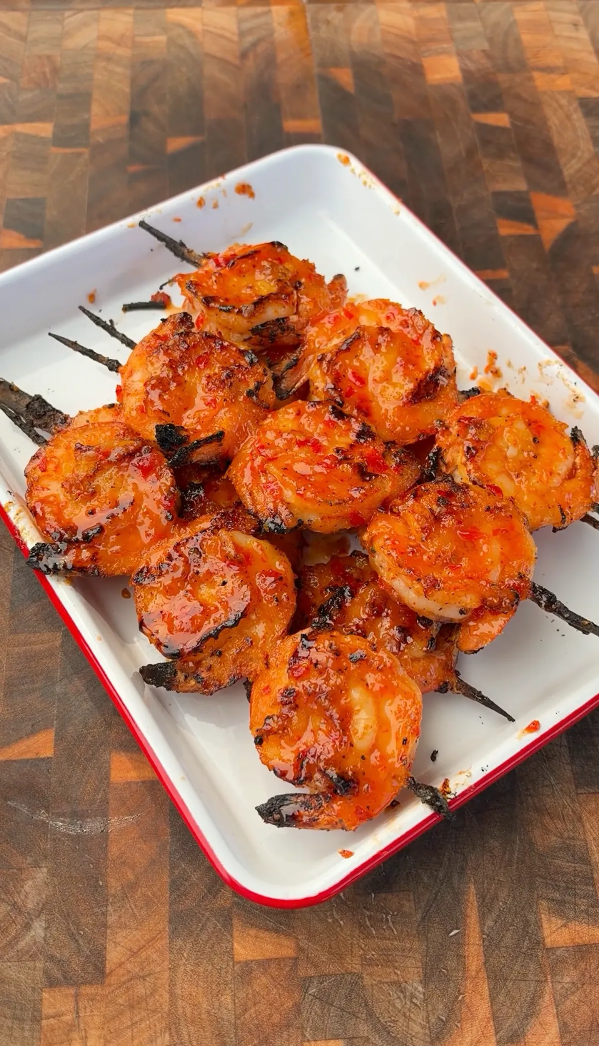 Firecracker glazed grilled shrimp skewers piled on a white enamel tray with sticky sweet chili sriracha glaze