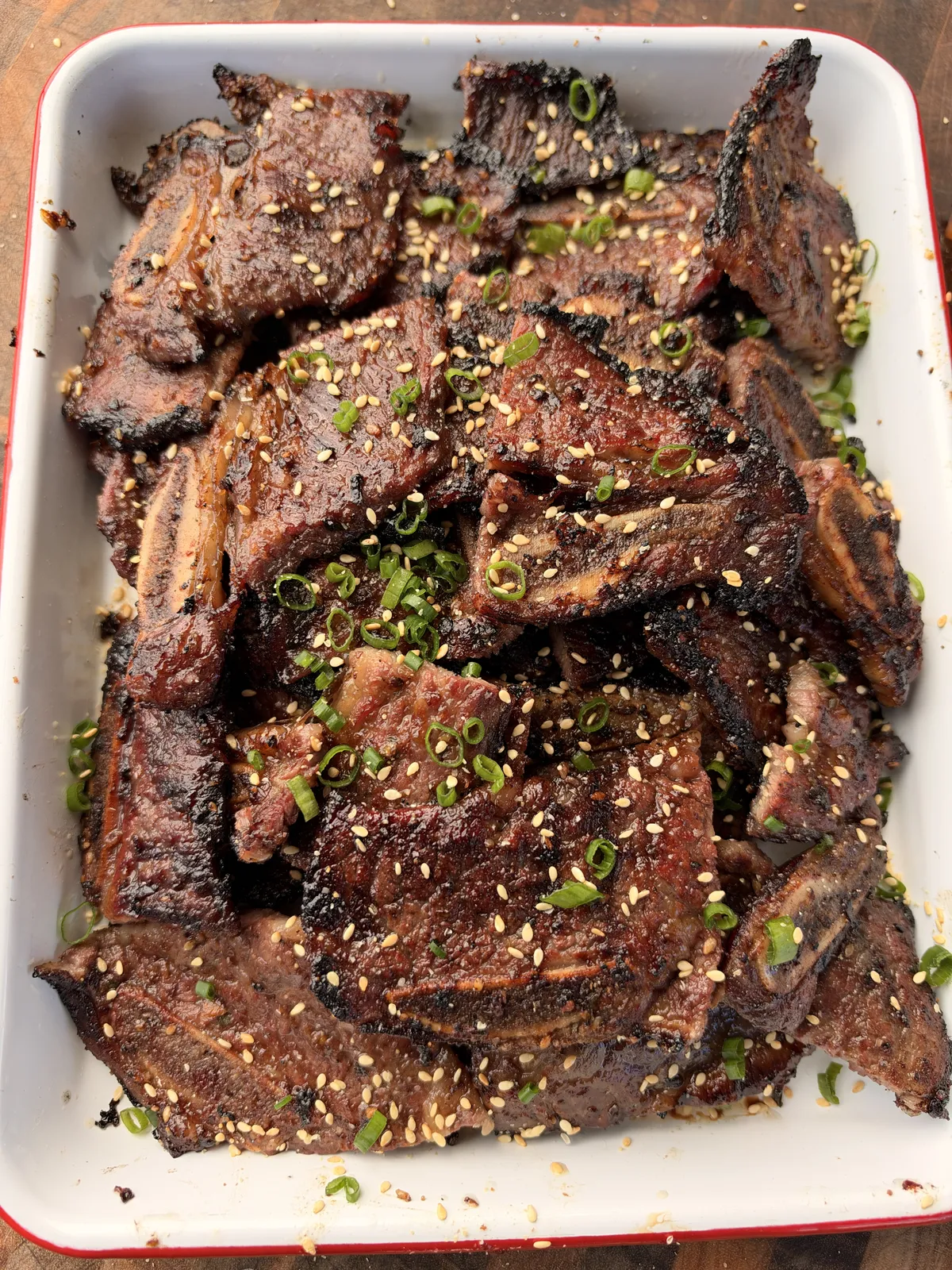 Flanken-cut Korean Kalbi beef short ribs piled in a white baking dish, topped with sliced green onions and toasted sesame seeds