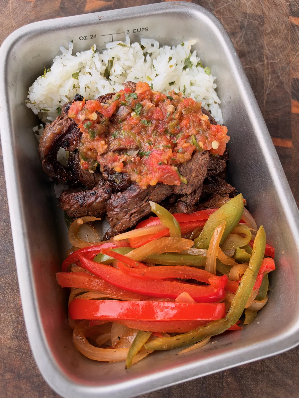 Meal prep container with grilled skirt steak topped with homemade salsa, cilantro lime rice, and charred bell peppers and onions