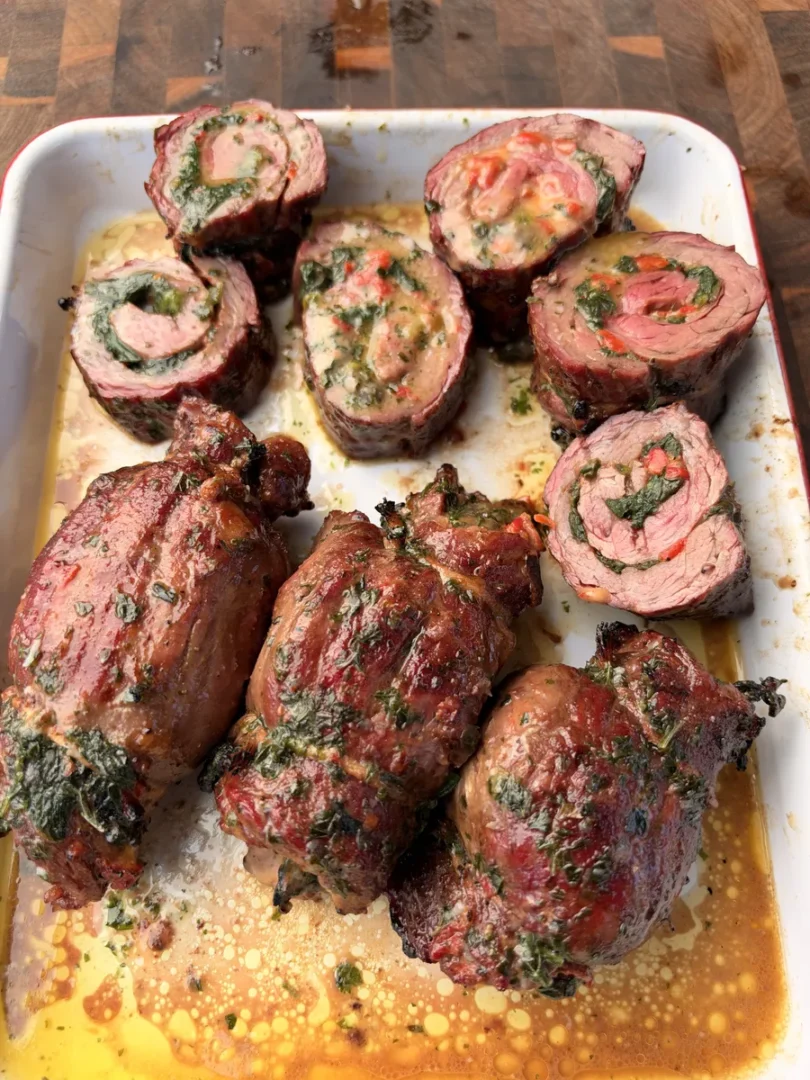 Grilled skirt steak pinwheels in baking dish, sliced open to reveal spinach, roasted red pepper, and Colby Jack filling