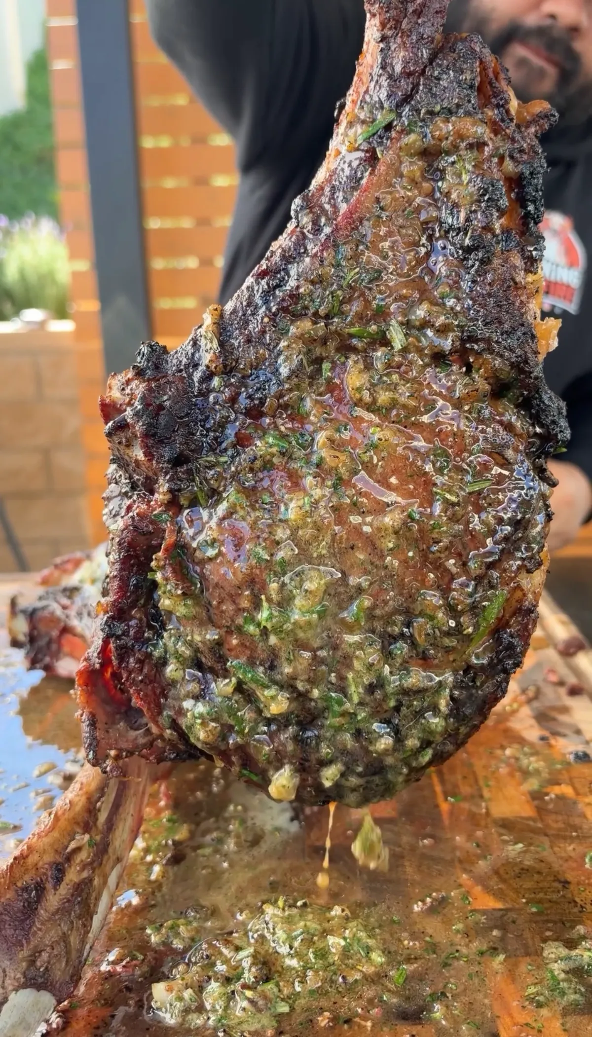 Two bone prime rib tomahawk held upright by the bones, coated in roasted garlic and herb compound butter melting over the crust