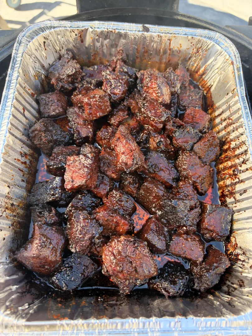 Smoked chuck roast burnt ends glazed in sticky honey BBQ sauce and butter in a foil pan