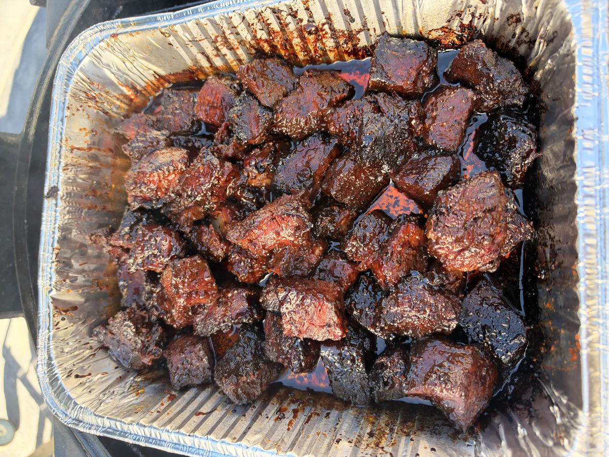 Smoked chuck roast burnt ends glazed in sticky honey BBQ sauce and butter in a foil pan
