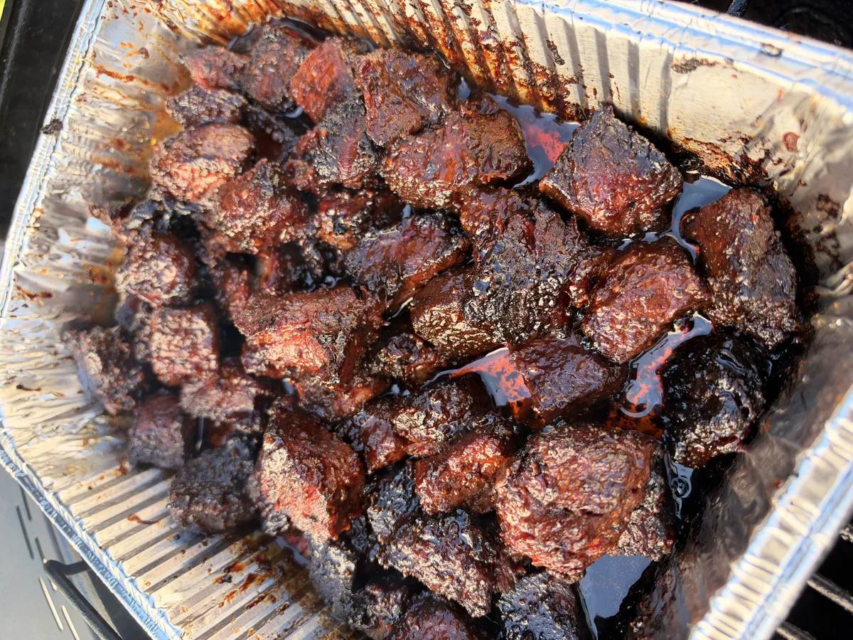 Honey BBQ smoked chuck roast burnt ends glazed in sticky hot honey BBQ sauce in a foil pan