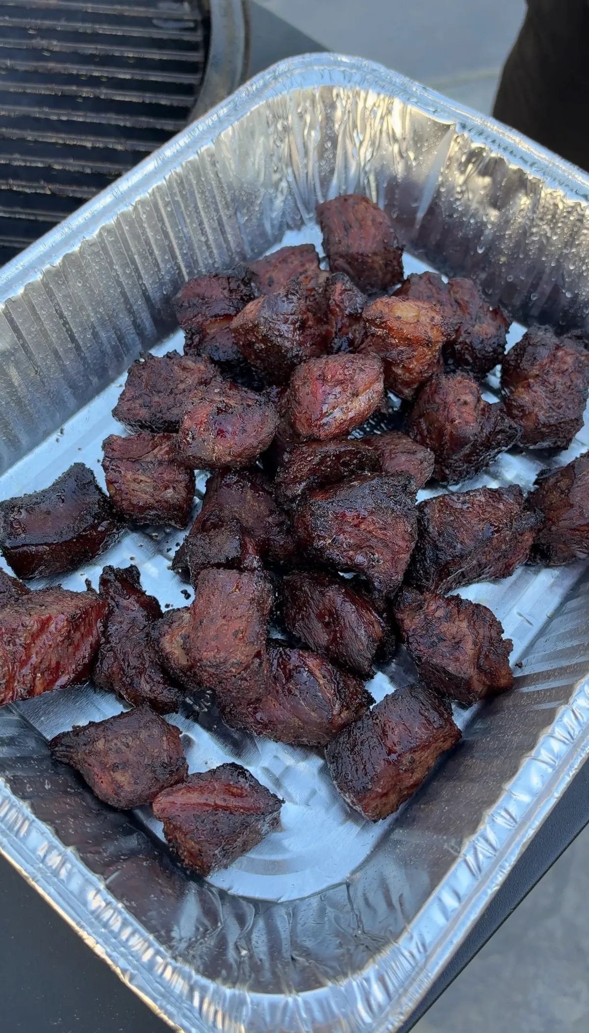Honey BBQ smoked chuck roast burnt ends glazed in sticky hot honey BBQ sauce in a foil pan
