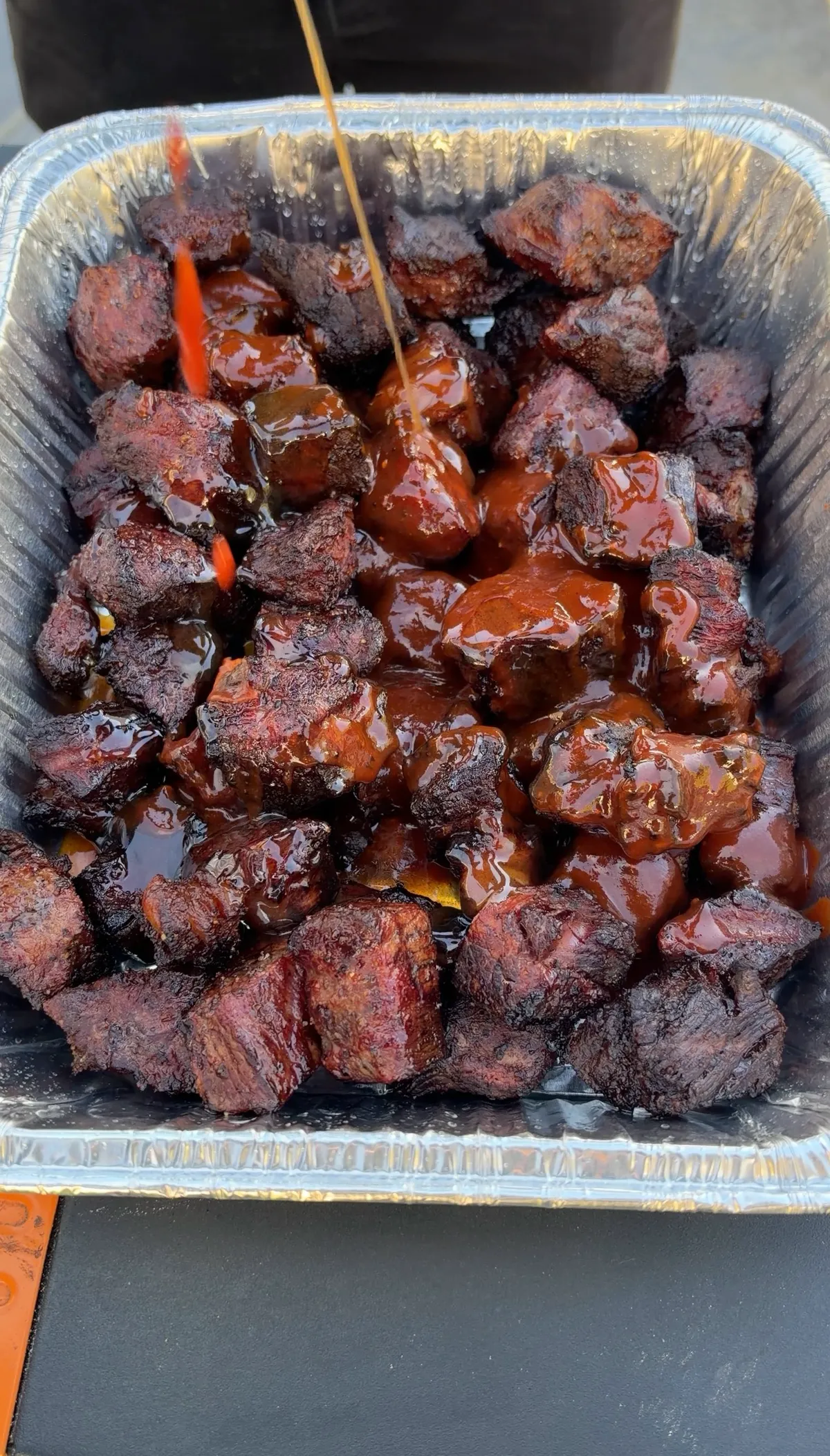 Smoked chuck roast burnt ends glazed in sticky honey BBQ sauce with butter in a foil pan