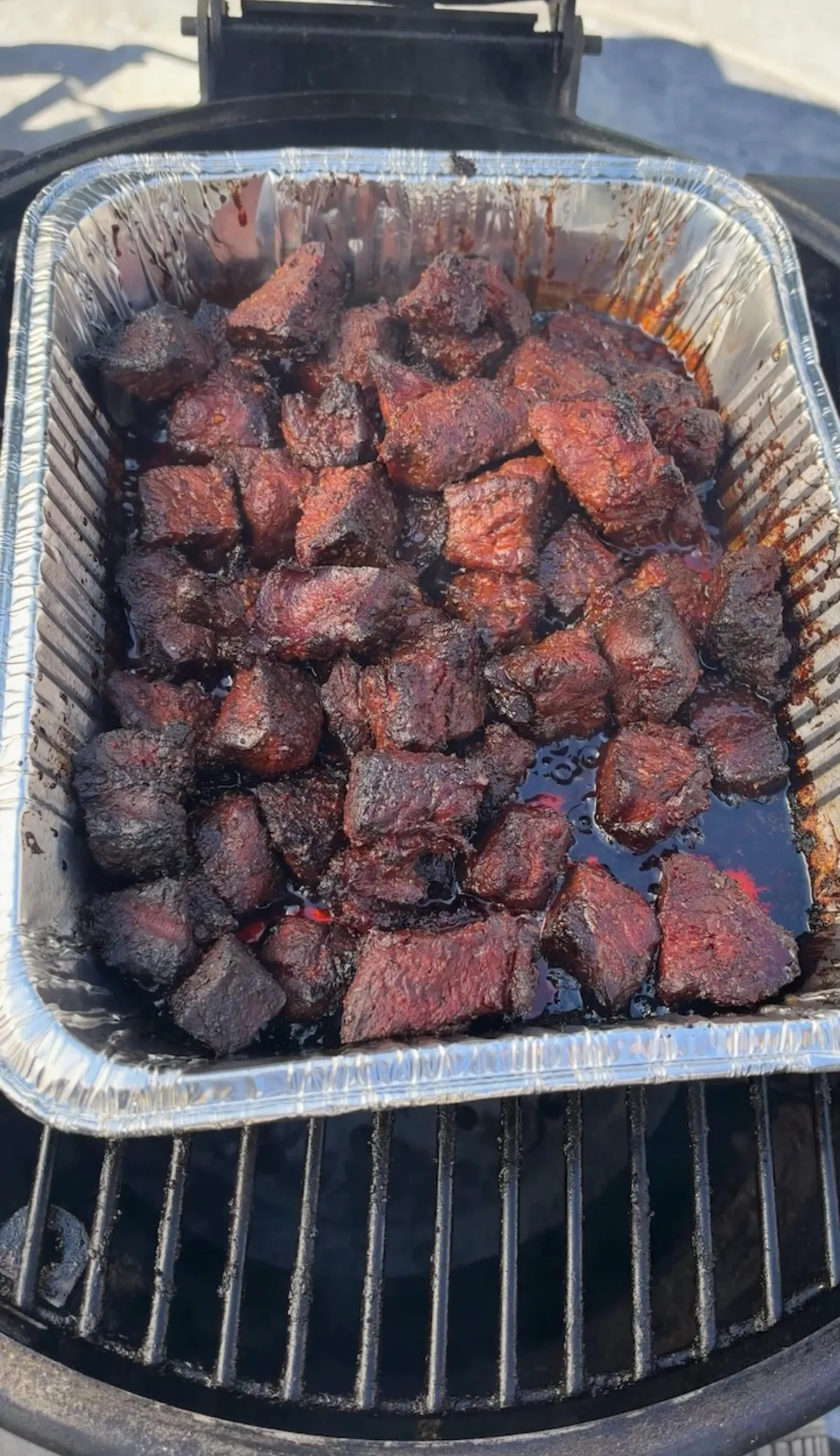 Smoked chuck roast burnt ends glazed in honey BBQ sauce and butter in a foil pan on a smoker grate
