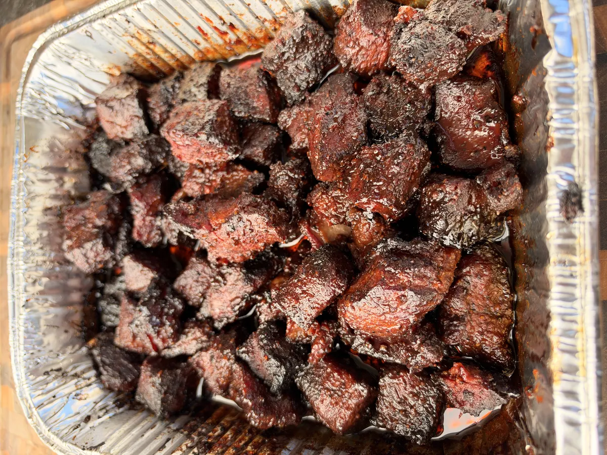 Honey BBQ smoked chuck roast burnt ends glazed in sticky hot honey BBQ sauce in a foil pan