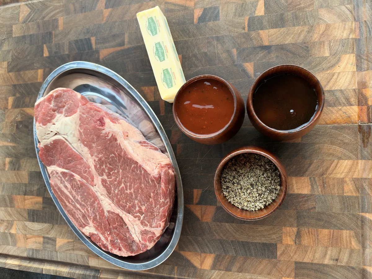 Chuck roast, Kerrygold butter, BBQ sauce, hot honey, and black pepper on a wood cutting board