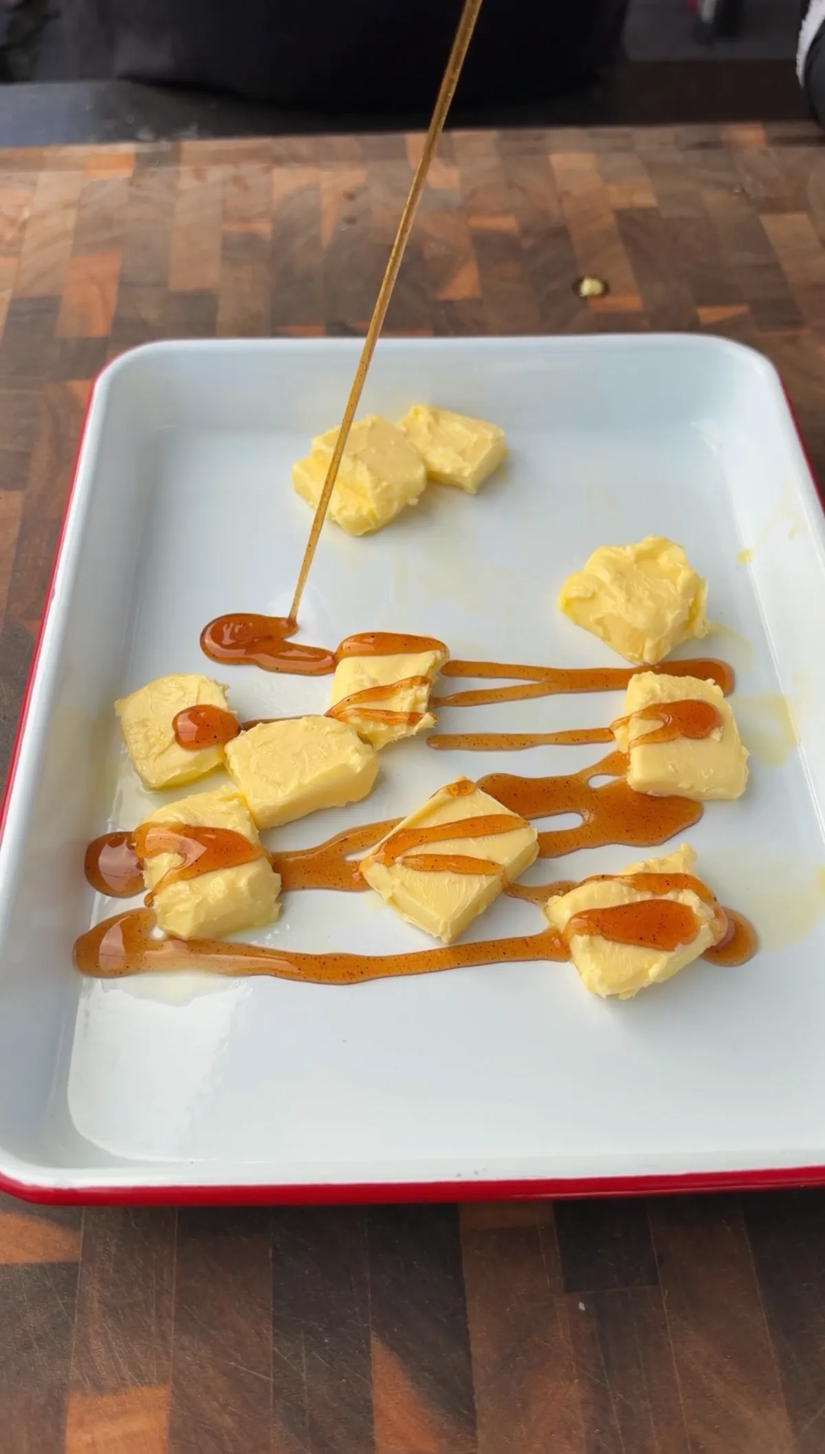 Hot honey being drizzled over unsalted butter pats in a white enamel tray for smoked turkey breast honey butter finish