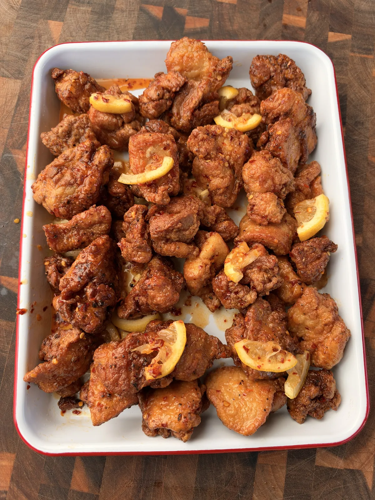 Crispy fried chicken thigh nuggets coated in hot honey lemon pepper sauce with lemon quarters and chili oil in a white tray