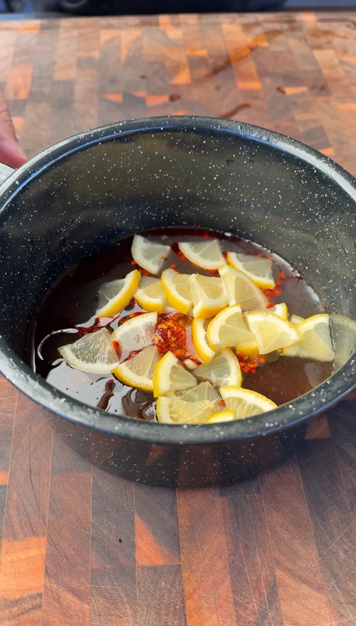 Hot honey lemon pepper sauce with chili oil and quartered lemon slices warming in a dark saucepan
