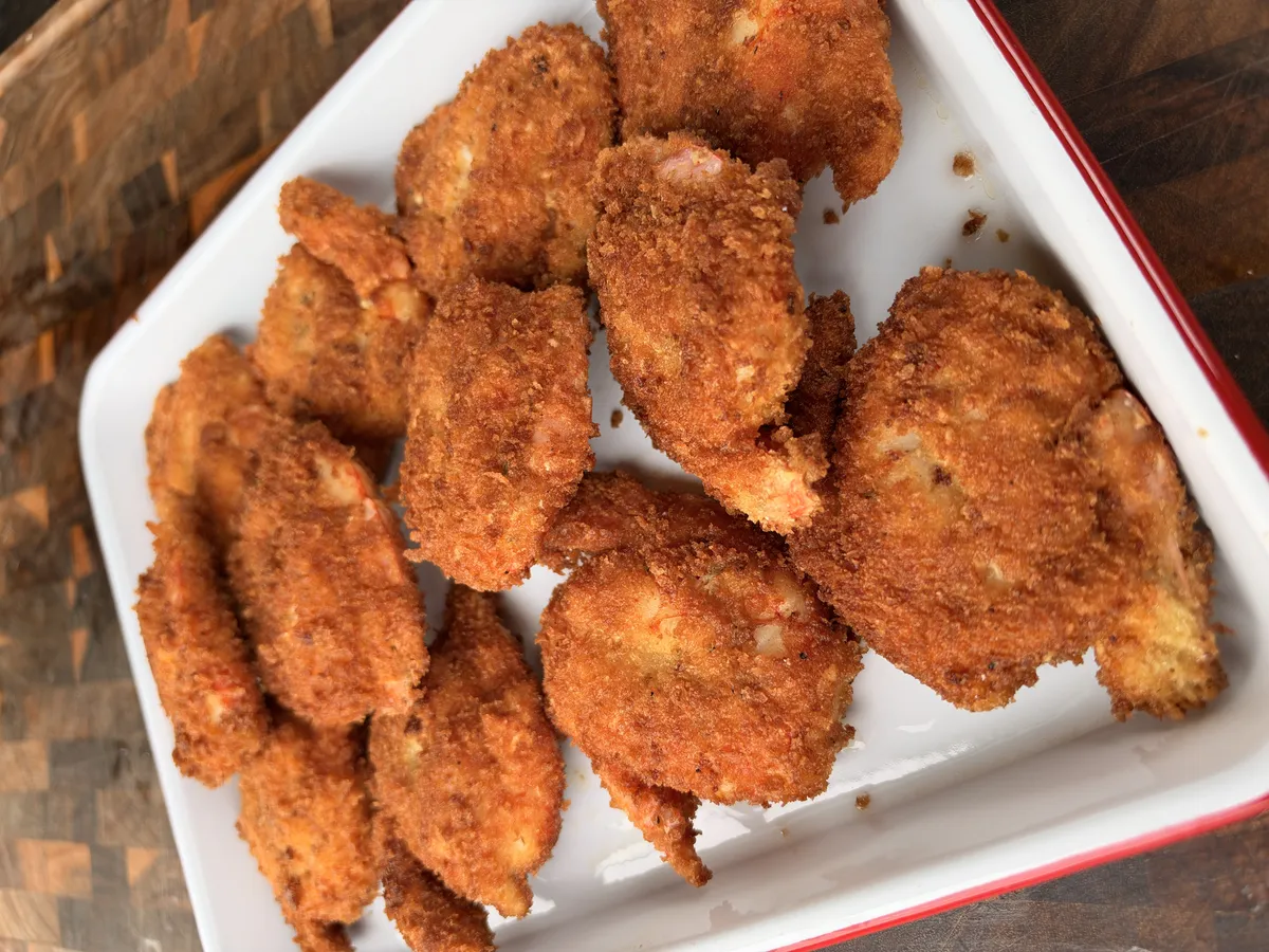 Crispy golden panko-breaded hot honey fried shrimp piled on a white dish with red trim