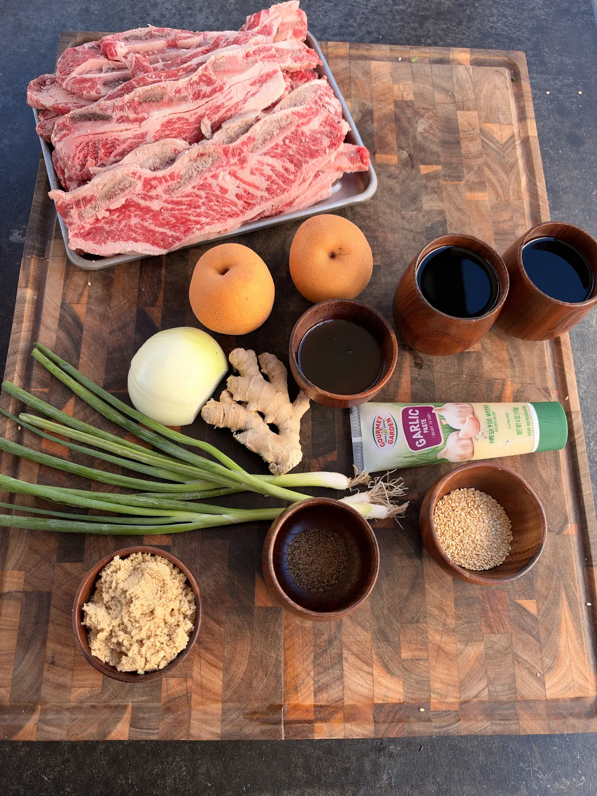 Flanken-cut beef short ribs with Asian pears, soy sauce, brown sugar, ginger, garlic paste, sesame seeds, and green onions on a wooden cutting board