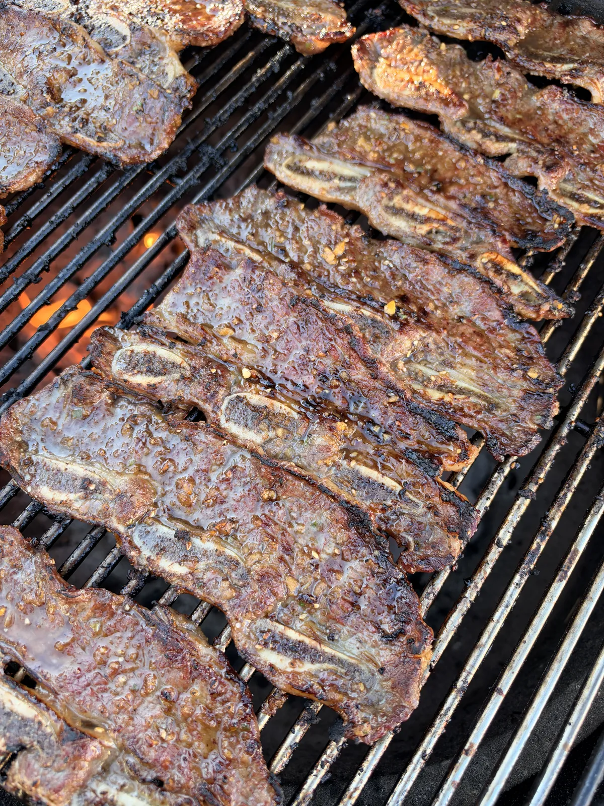 Flanken-cut Korean Kalbi beef short ribs grilling over direct high heat, showing caramelized char and sesame marinade glaze
