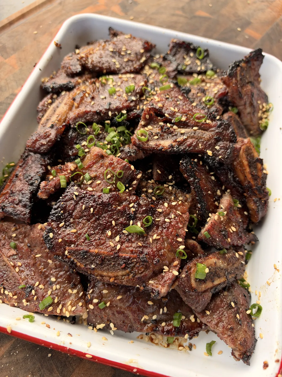 Grilled flanken-cut Korean kalbi beef short ribs garnished with toasted sesame seeds and sliced green onions in a white baking dish