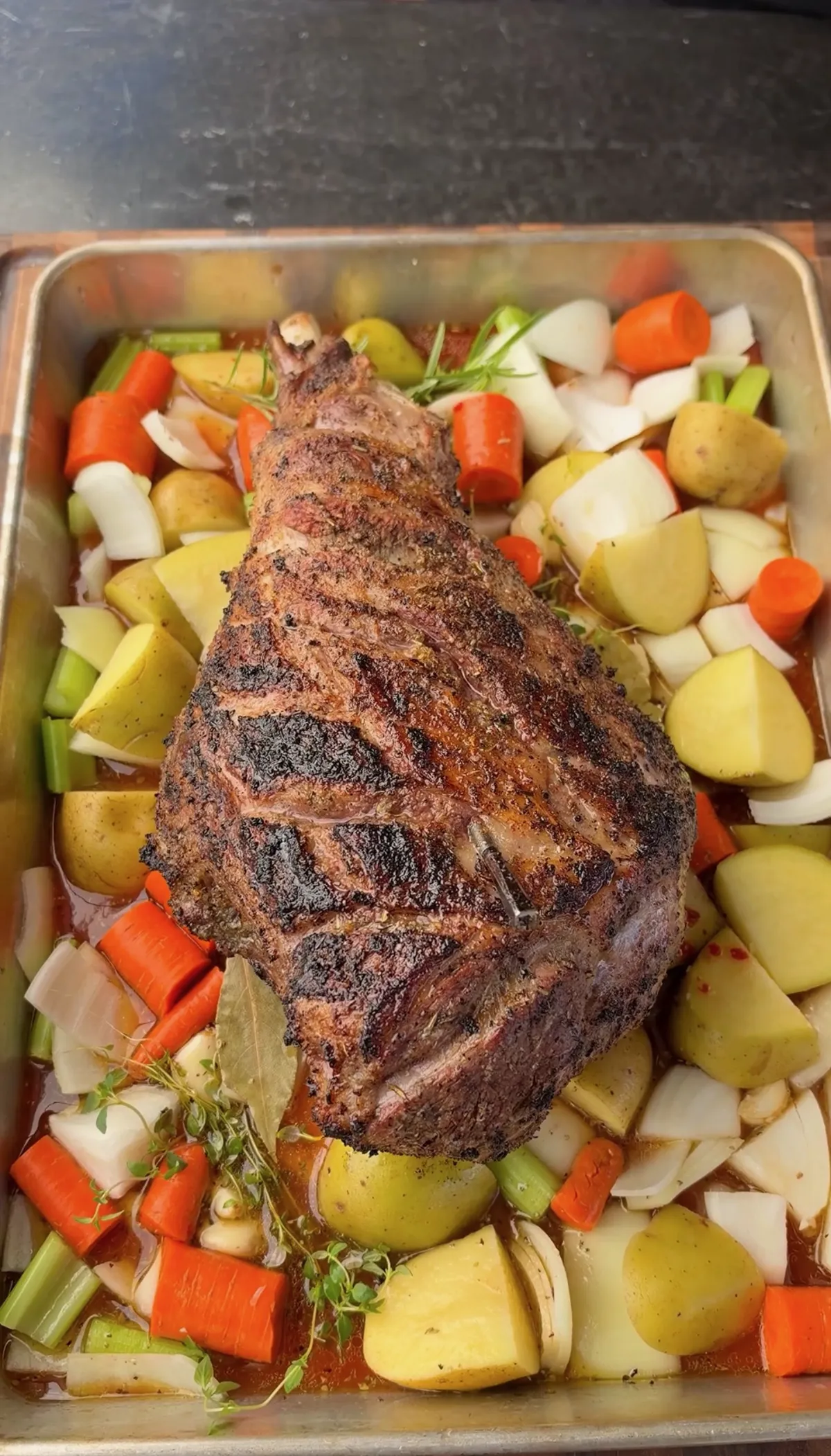 Seared leg of lamb nestled over Yukon Gold potatoes, carrots, celery, onions with fresh thyme and bay leaves in roasting pan