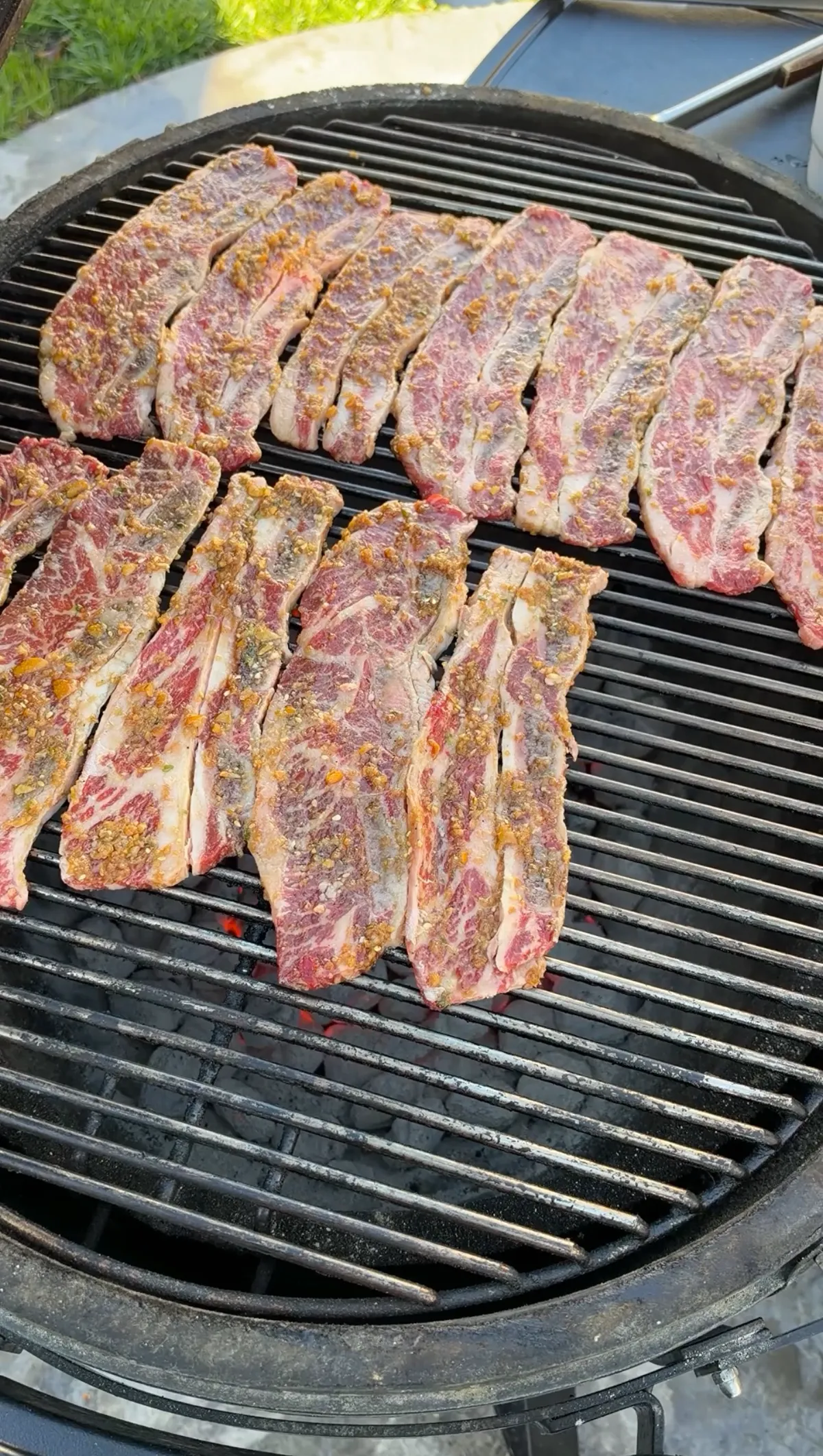 Raw kalbi-marinated flanken-cut beef short ribs arranged on a round charcoal grill over direct heat