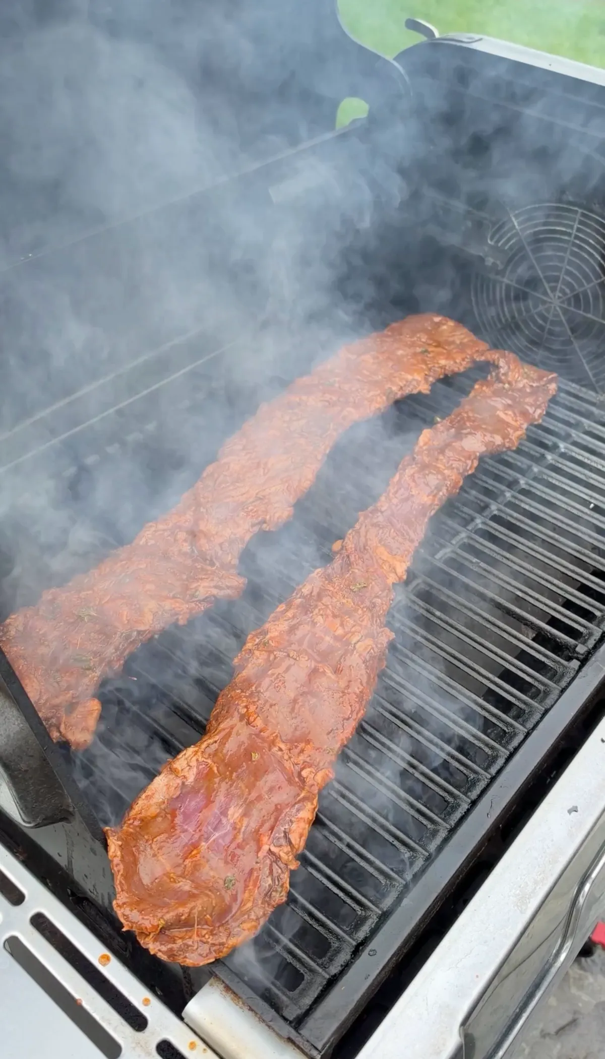 Two strips of citrus-marinated skirt steak smoking on a gas grill at high heat before charring