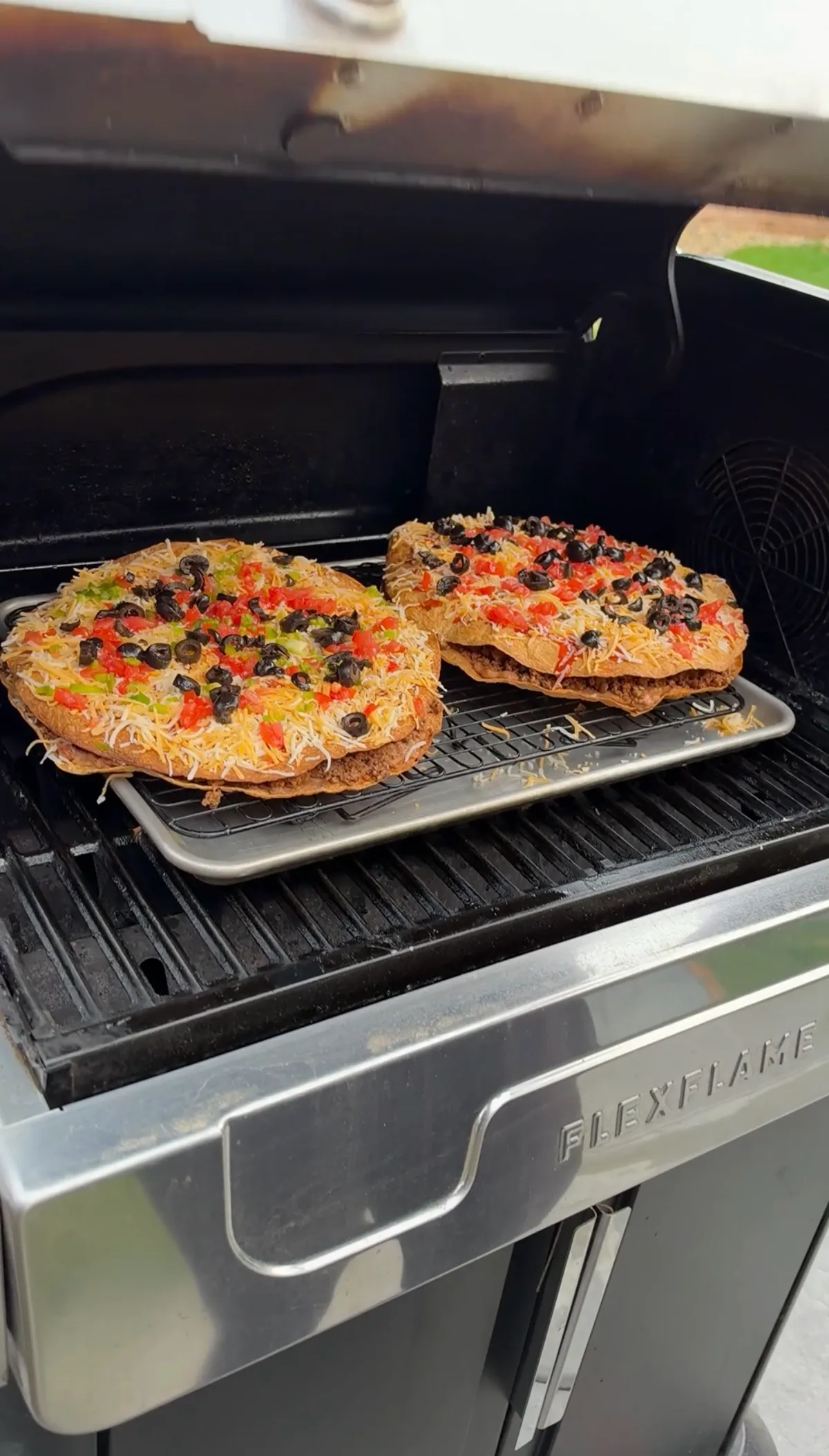 Two assembled taco bell mexican pizza copycat pies with Colby Jack, diced tomatoes, black olives and jalapeños melting on the grill