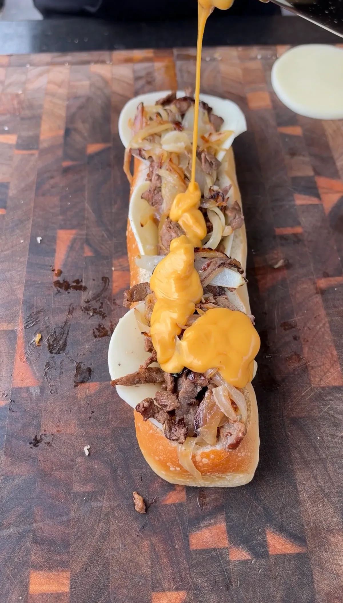Nacho cheese sauce drizzled over ribeye steak, caramelized onions, and provolone inside a hollowed French baguette