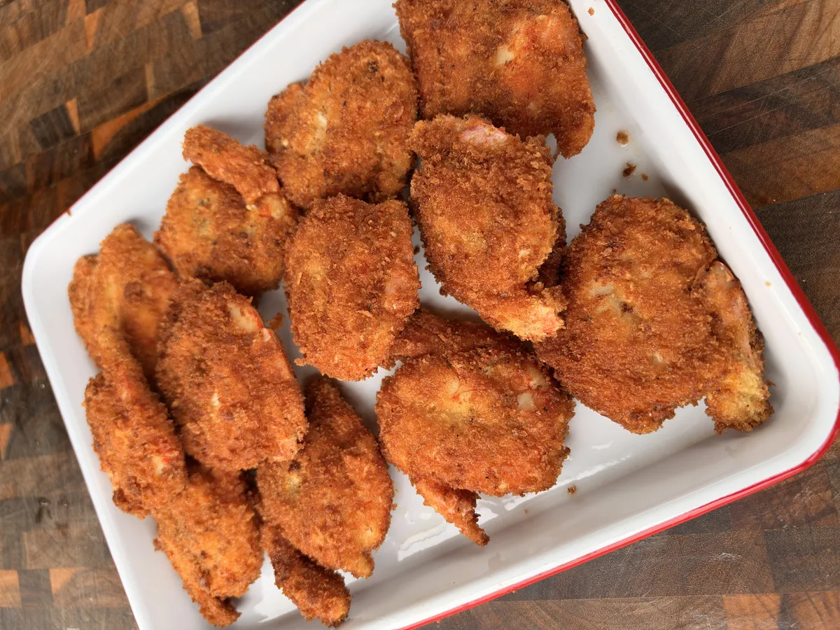 Crispy golden panko-breaded fried shrimp piled on a white and red enamel tray on a wooden surface