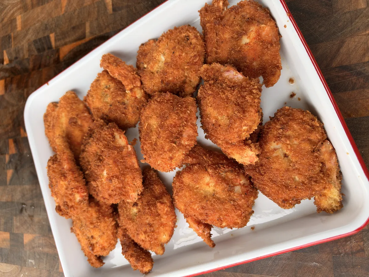 Crispy golden panko-breaded fried shrimp arranged on a white enamel serving platter on a wooden board