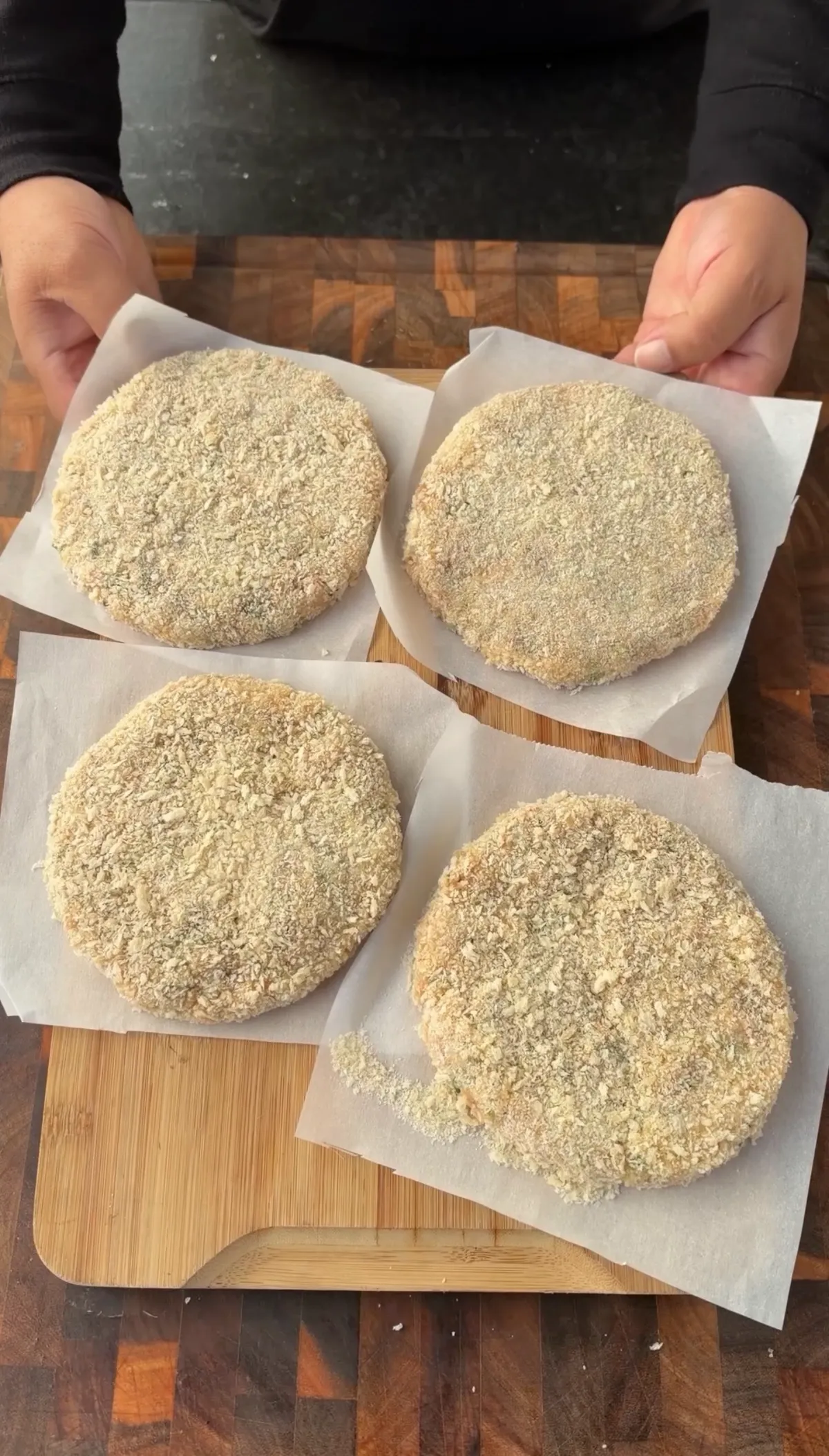 Four panko-breaded raw shrimp burger patties on parchment paper squares, ready to fry