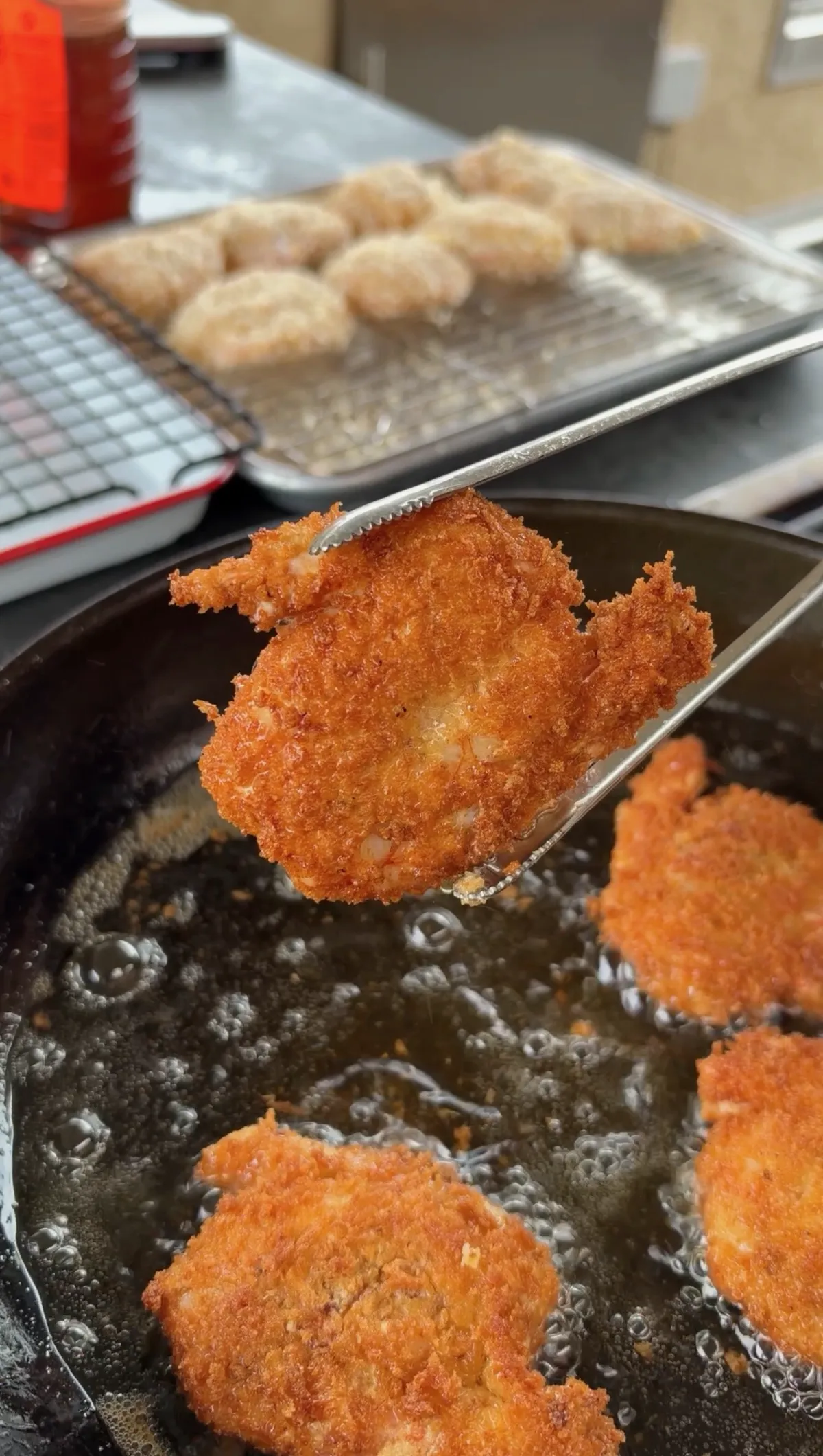 Crispy golden panko-breaded shrimp held with tongs over a skillet of hot oil at 350°F with more shrimp frying