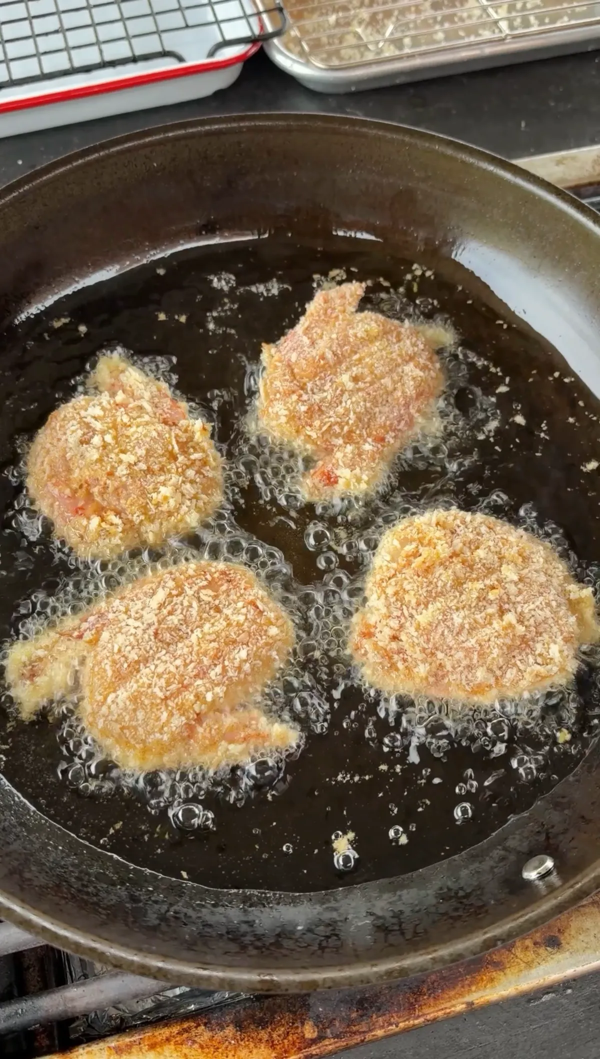 Four panko-breaded shrimp pairs frying in avocado oil in a dark skillet, golden and crispy