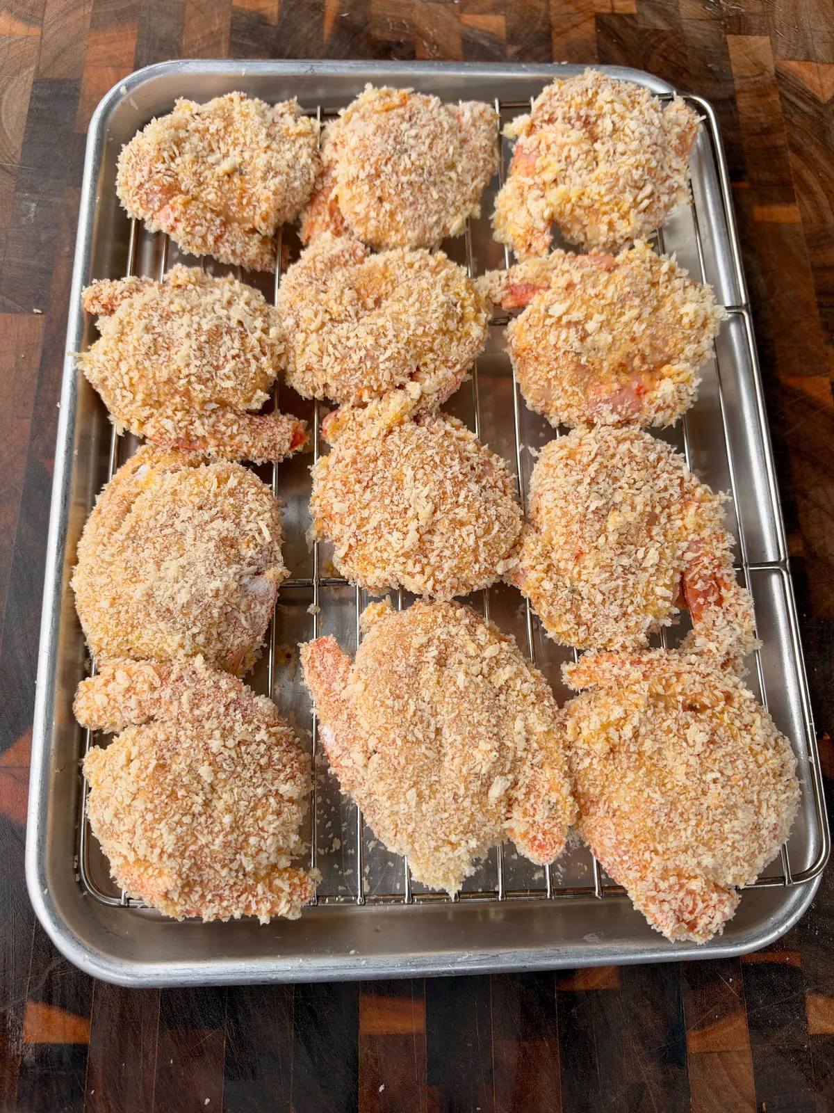 Raw panko-breaded shrimp pairs on a wire rack over a baking sheet, ready to fry