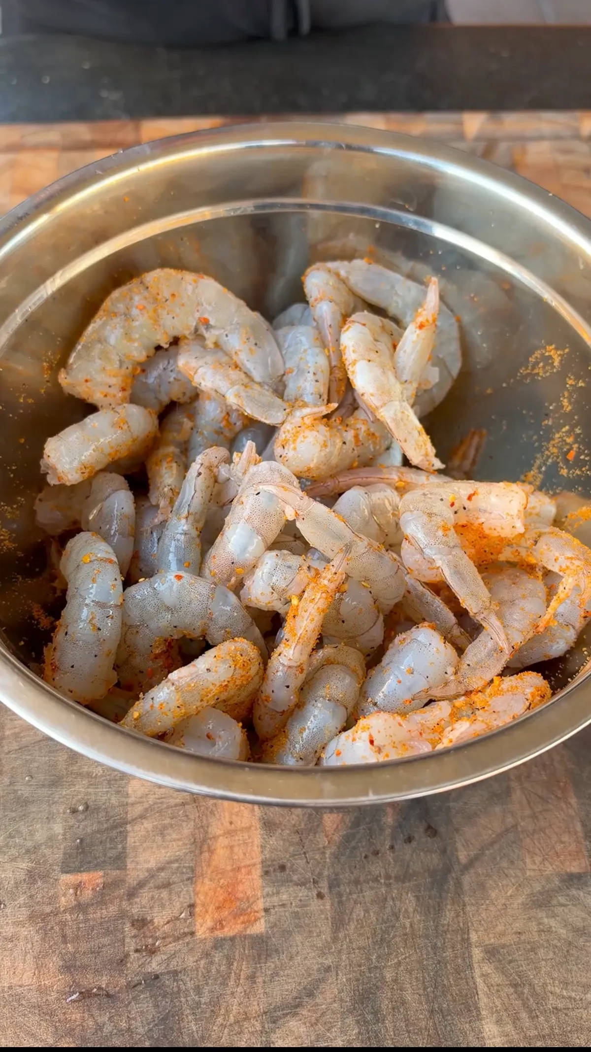 Raw peeled and deveined shrimp tossed with Cajun seasoning in a stainless steel mixing bowl