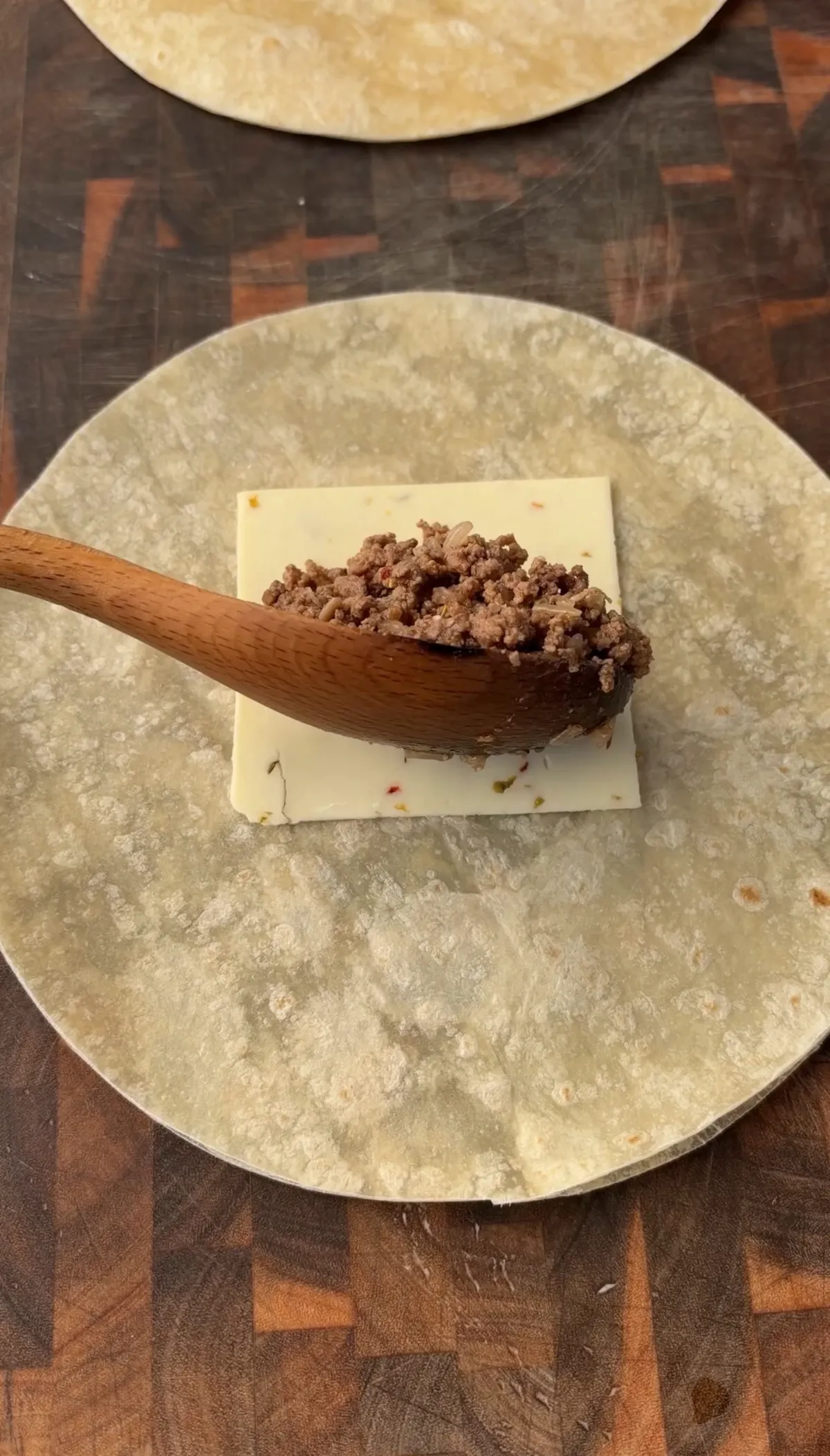 Slice of pepper jack cheese topped with seasoned 85/15 ground beef on a 10-inch flour tortilla, ready to fold
