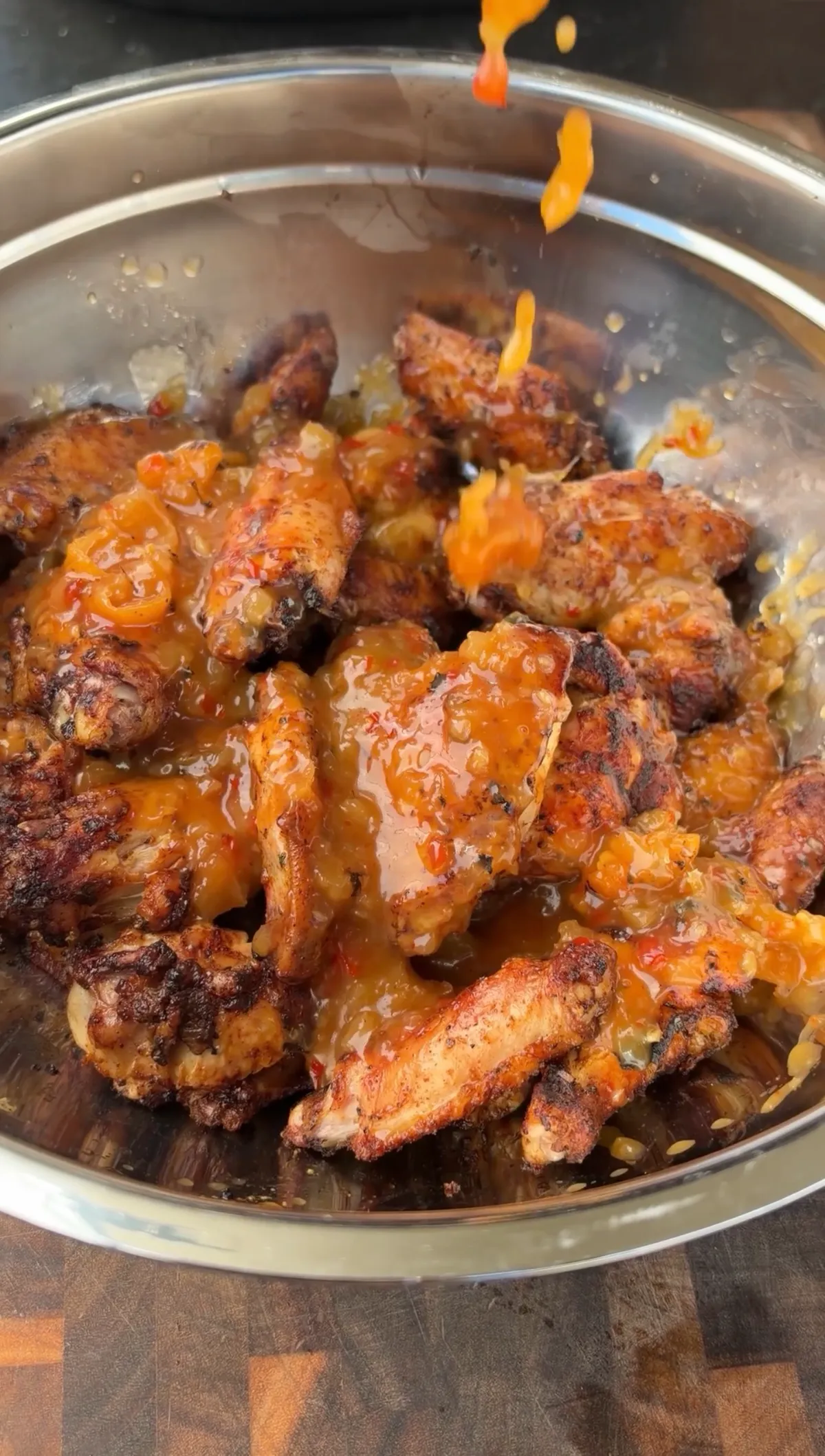 Grilled chicken wings in a stainless steel bowl being tossed in sticky pineapple habanero glaze with crushed pineapple
