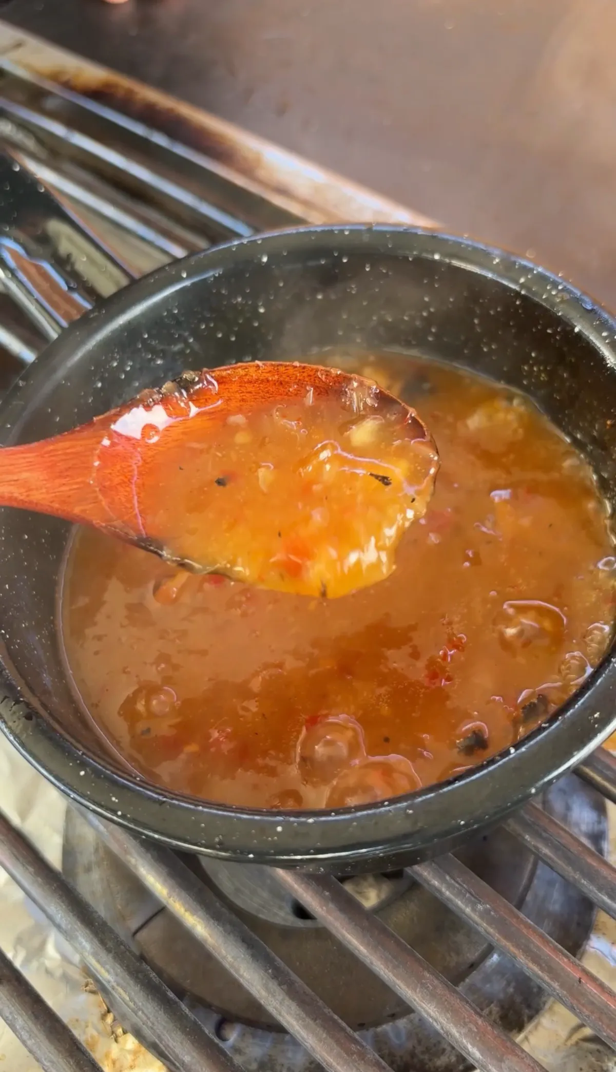 Pineapple habanero glaze simmering in a dark saucepan on grill grates, stirred with a wooden spoon