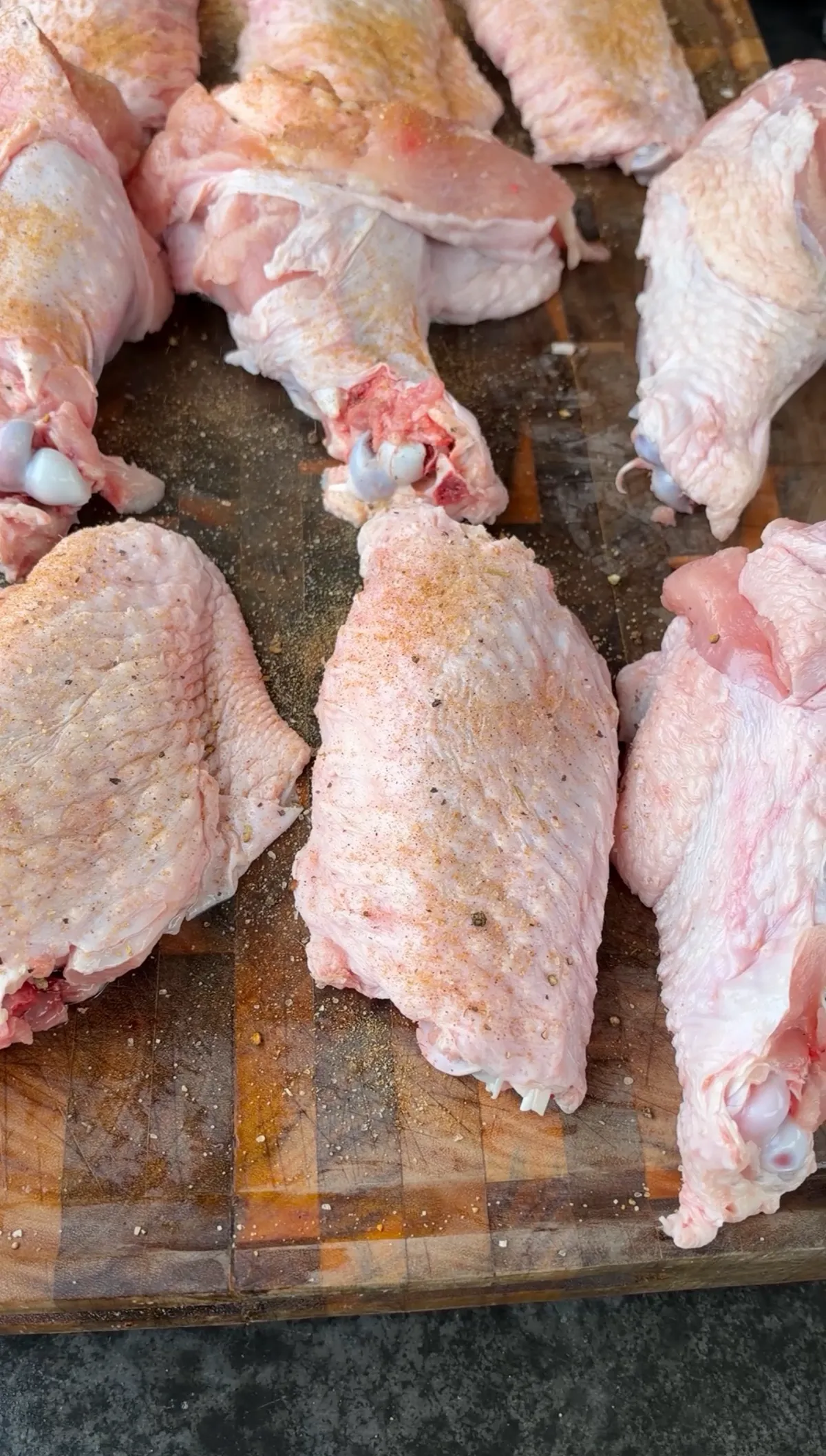 Raw turkey wing drumettes and flats generously coated with poultry seasoning on a wooden cutting board