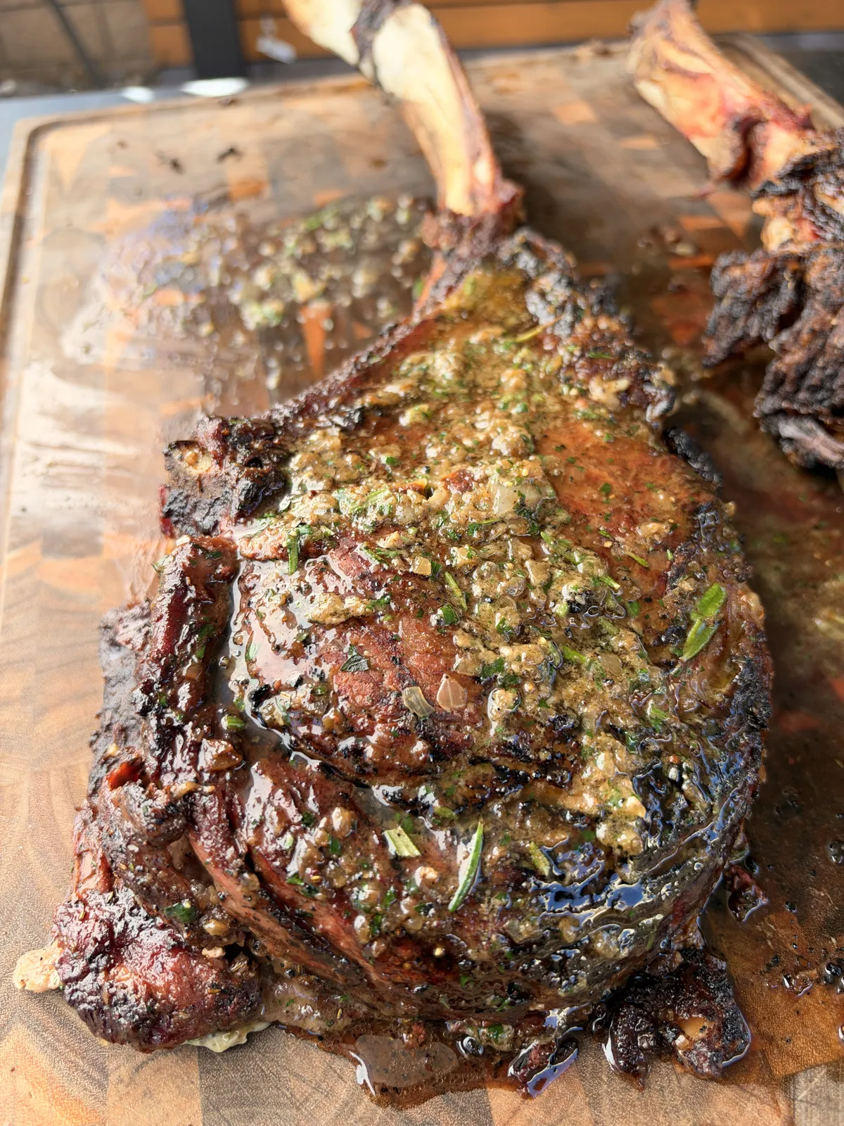 Two-bone prime rib tomahawk topped with roasted garlic and onion compound butter melting over seared crust on wooden cutting board