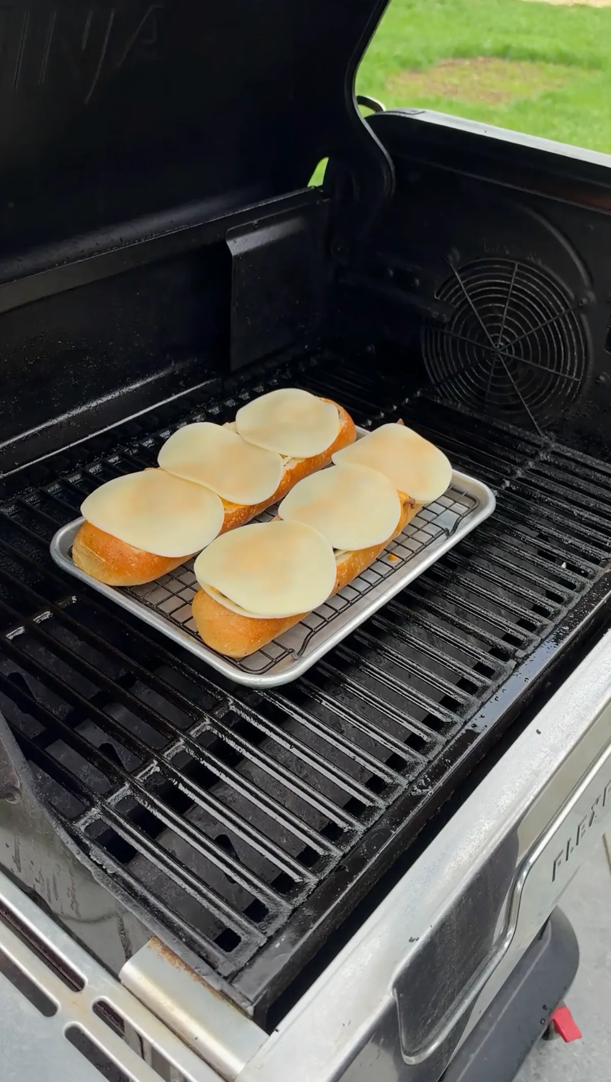 Provolone cheese slices layered over hollowed French baguette halves on a wire rack baking sheet on a grill
