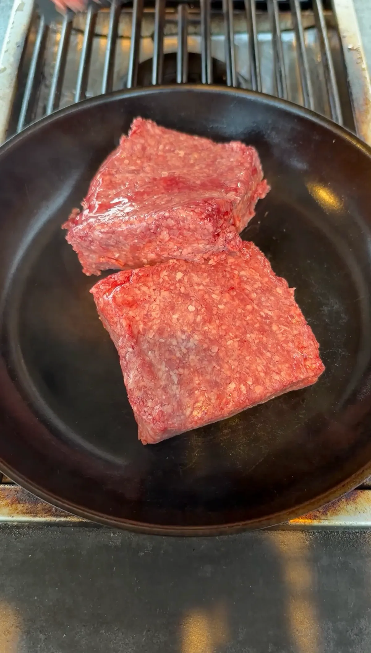 Two raw 85/15 ground beef portions in a black skillet, ready to cook for Taco Bell copycat Mexican pizza