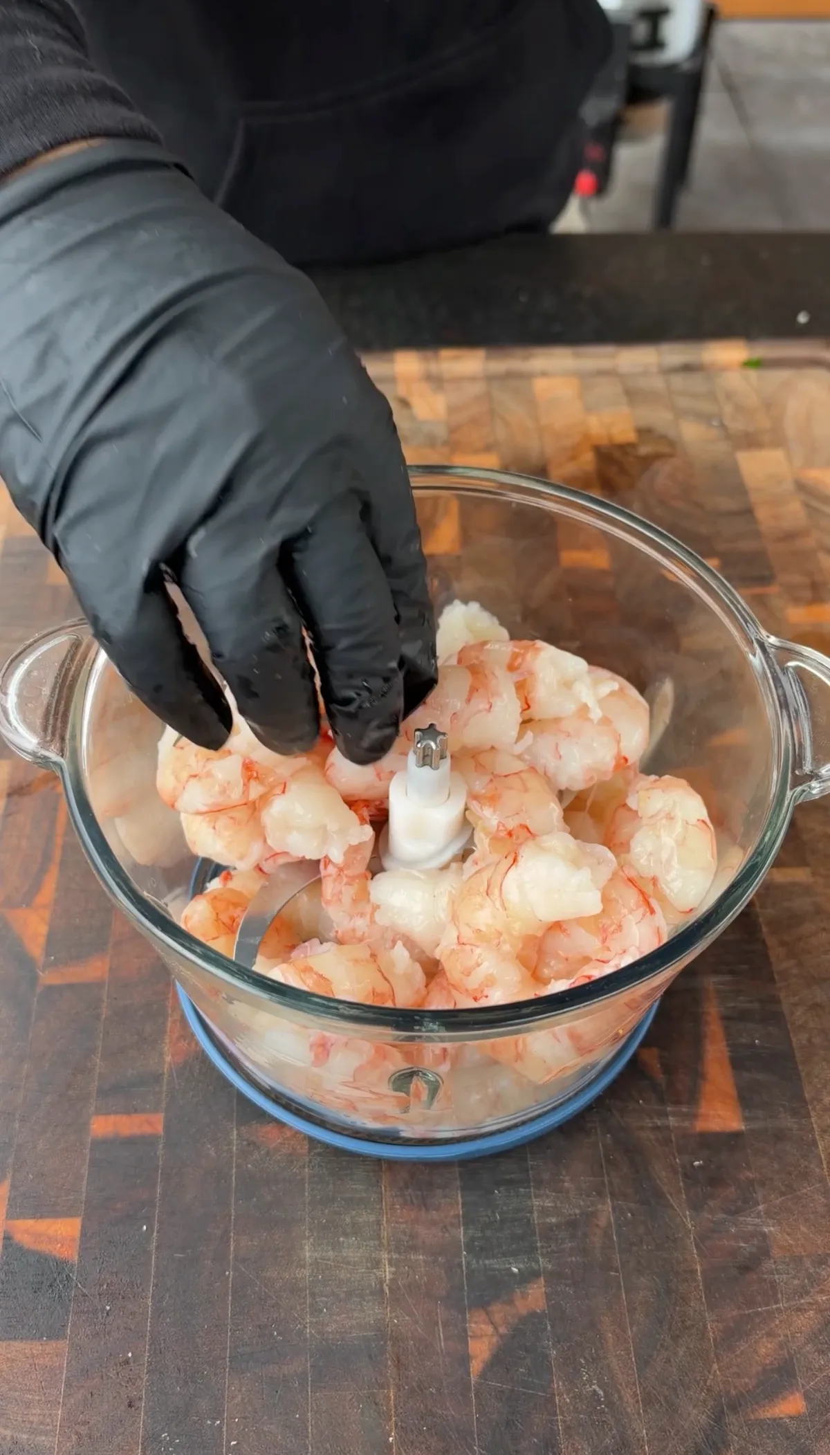 Gloved hands placing peeled and deveined raw Argentine shrimp into a food processor bowl to pulse for shrimp burger patties