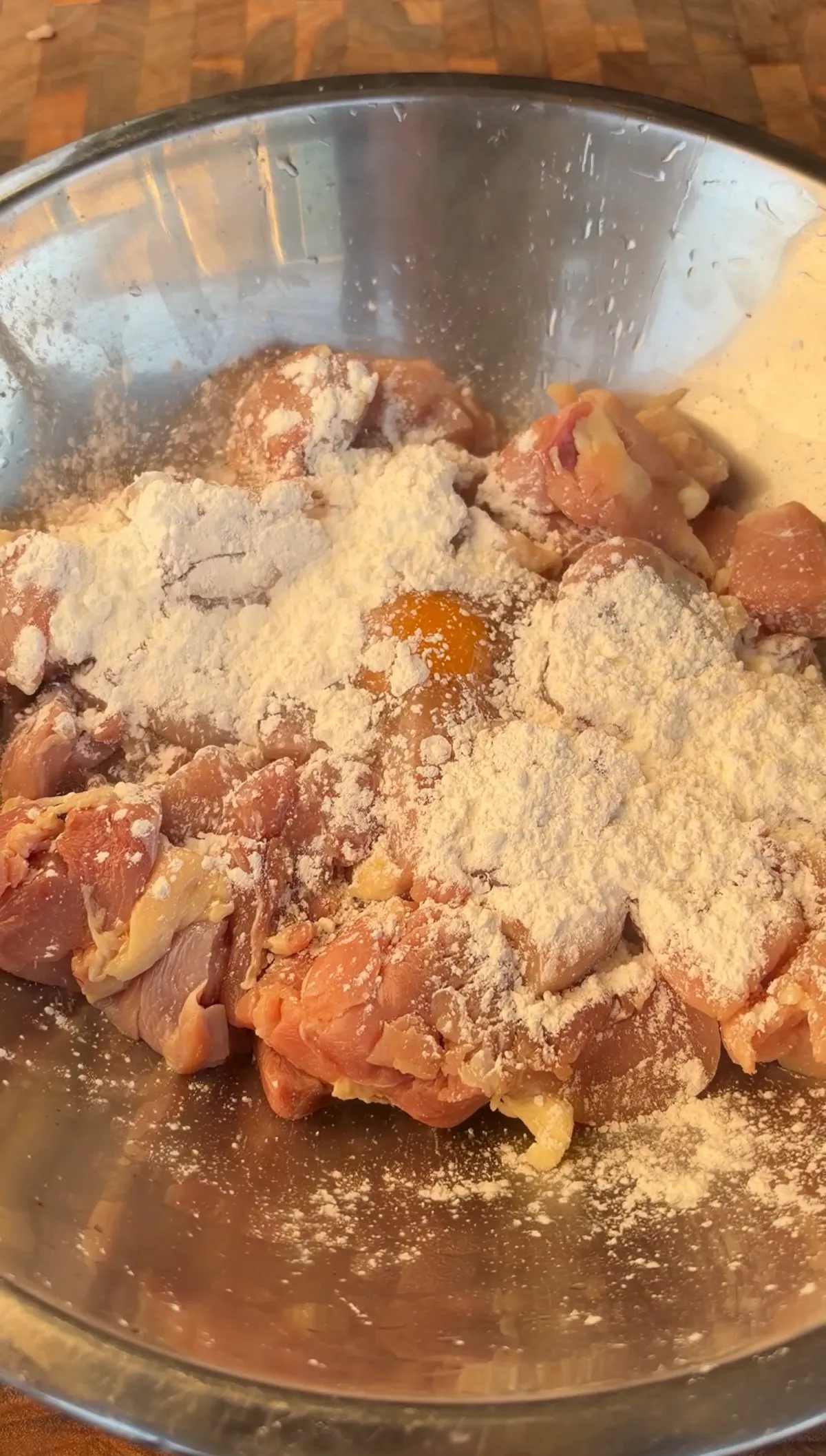 Raw chicken thigh pieces dusted with all-purpose flour in a stainless steel mixing bowl, ready to fry
