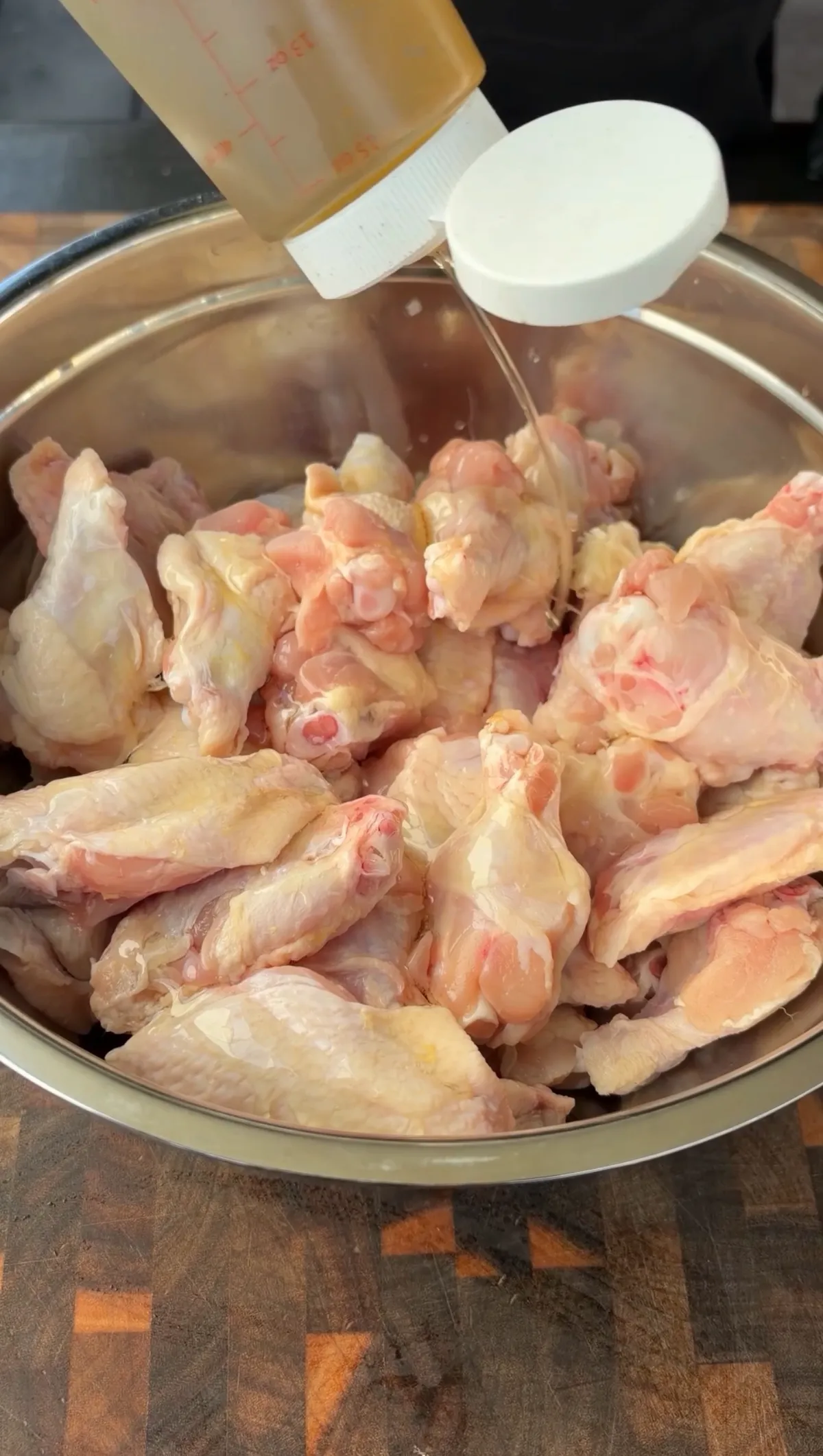 Raw chicken wing flats and drumettes in a stainless steel bowl being drizzled with olive oil before seasoning