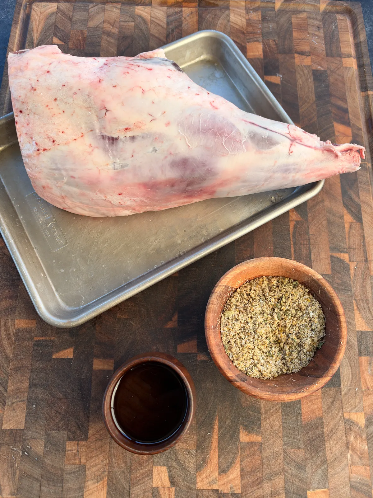 Raw leg of lamb on a sheet tray with Greek oregano spice rub and olive oil ready for seasoning