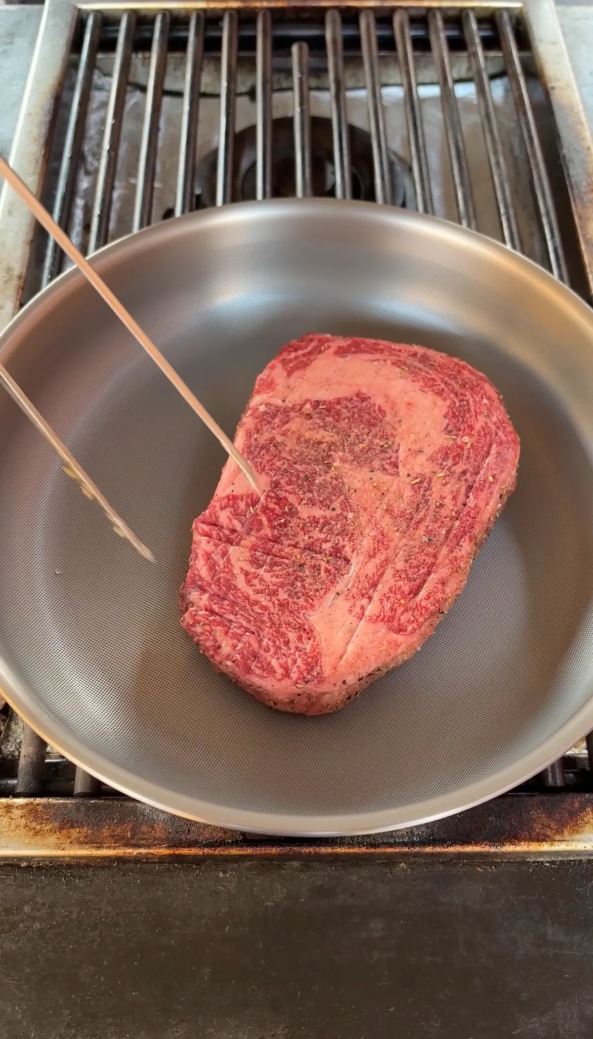 Raw ribeye steak seasoned with steak seasoning placed in a stainless steel pan before searing