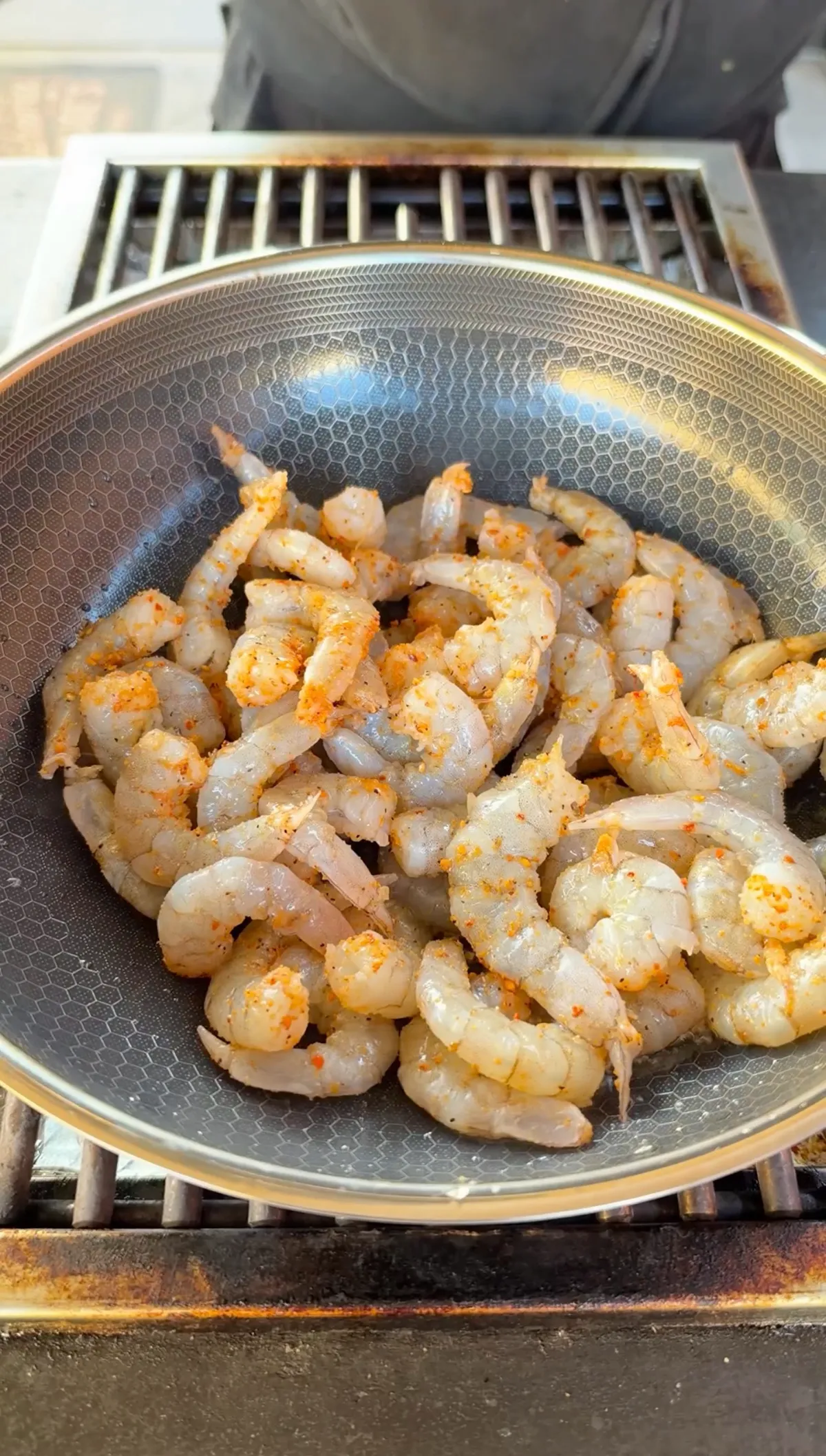 Raw shrimp seasoned with Cajun seasoning cooking in a stainless steel wok on a gas grill