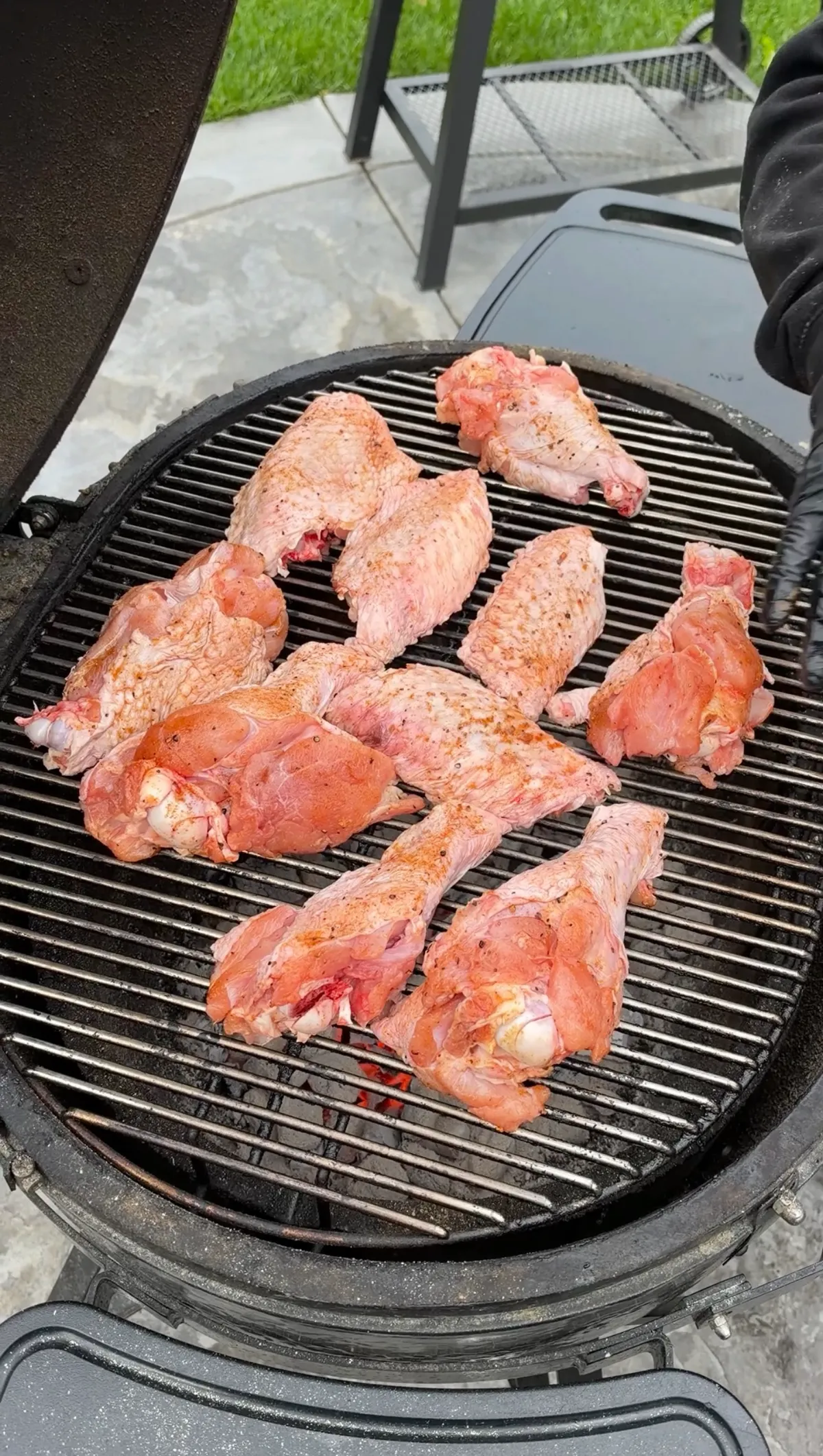 Raw turkey wing flats and drums coated in poultry seasoning arranged on a charcoal grill at the start of cooking