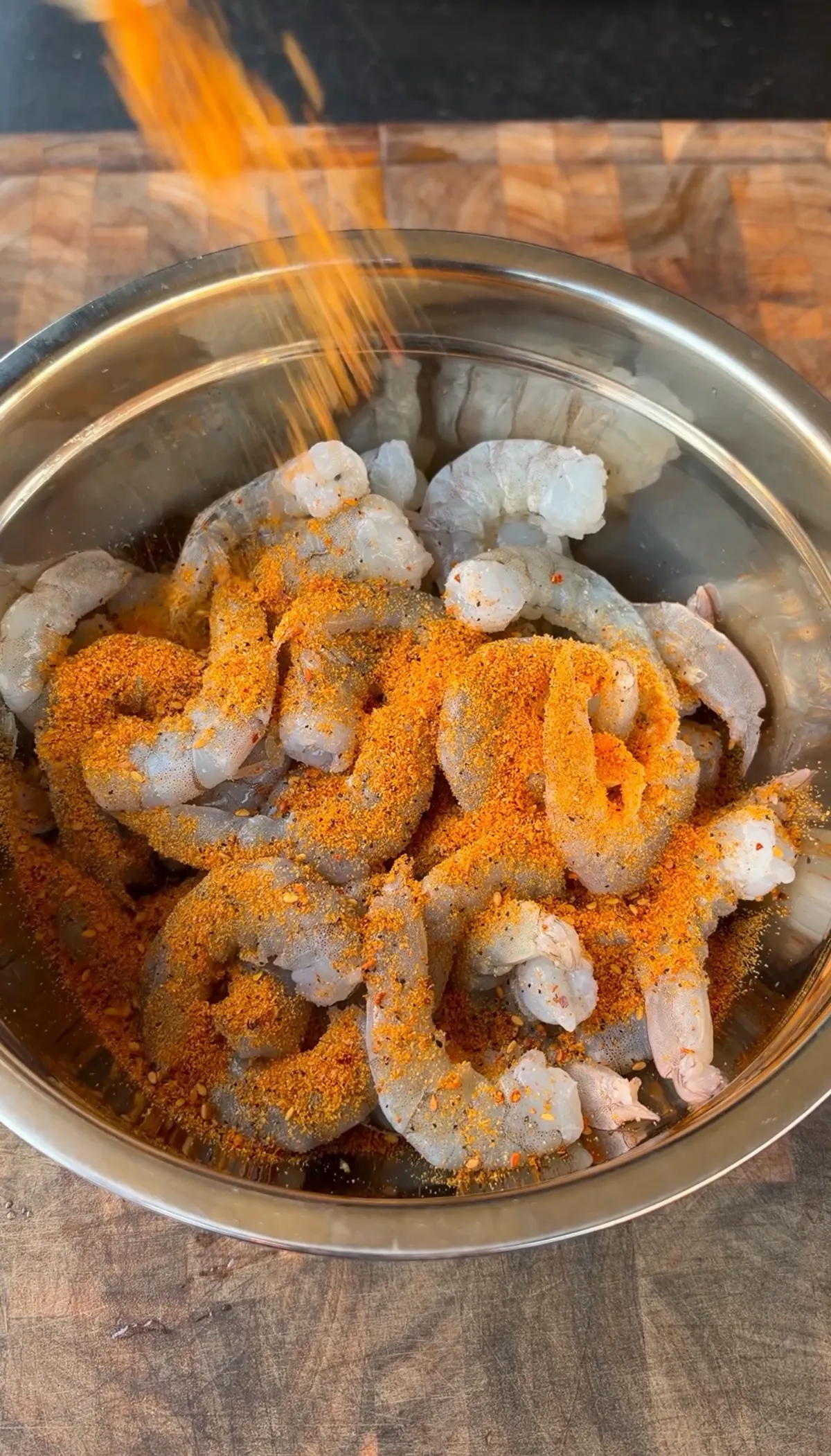 Raw peeled and deveined shrimp in a stainless steel bowl being coated with Cajun seasoning
