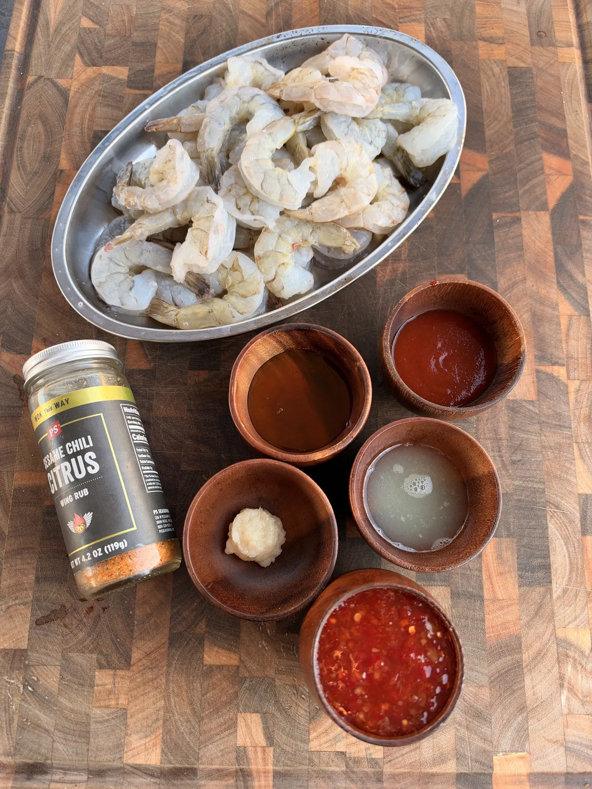 Raw peeled shrimp with sweet chili sauce, sriracha, honey, lime juice, and minced garlic prepped on a cutting board