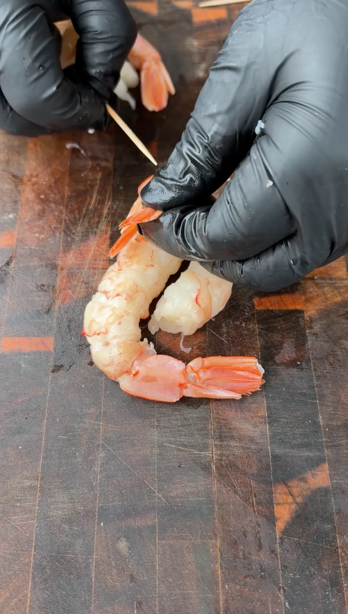 Two large raw peeled shrimp arranged in yin-yang shape, held together with a toothpick on a dark cutting board
