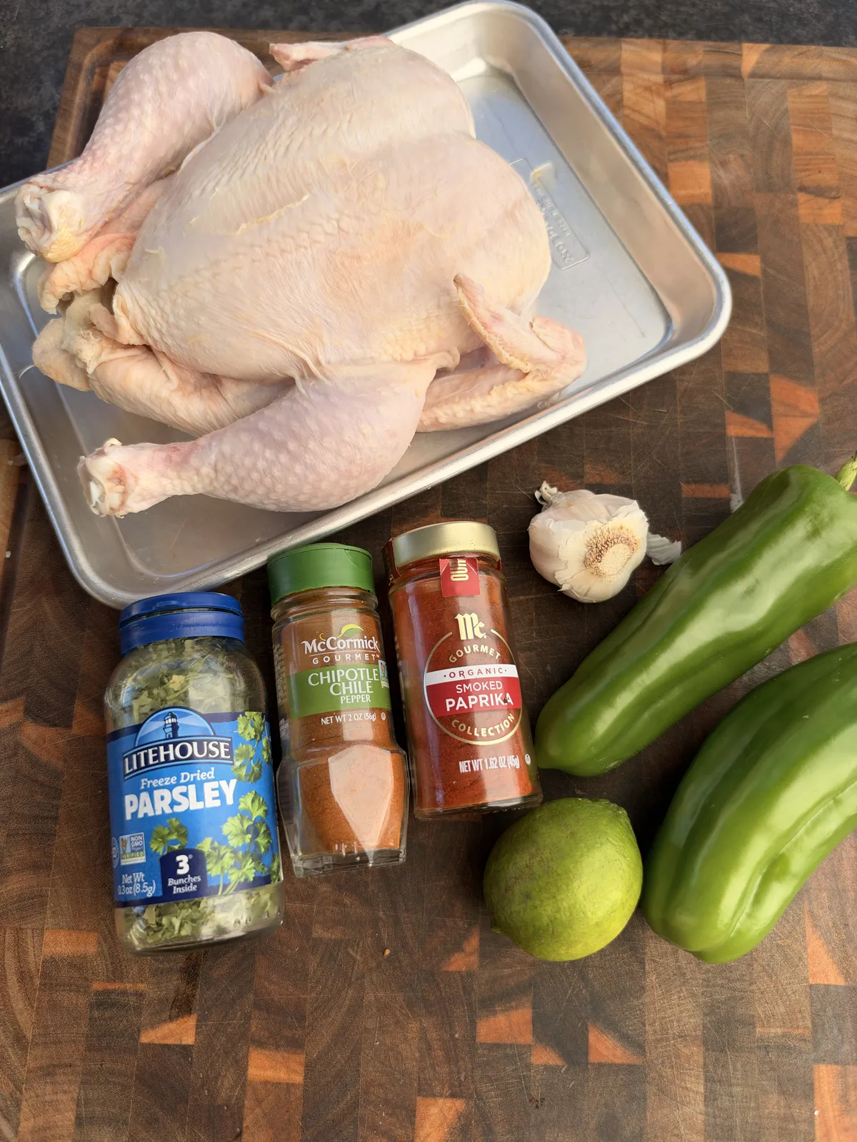 Raw spatchcocked whole chicken on a tray with green chiles, lime, garlic, chipotle chile pepper, smoked paprika, and dried parsley